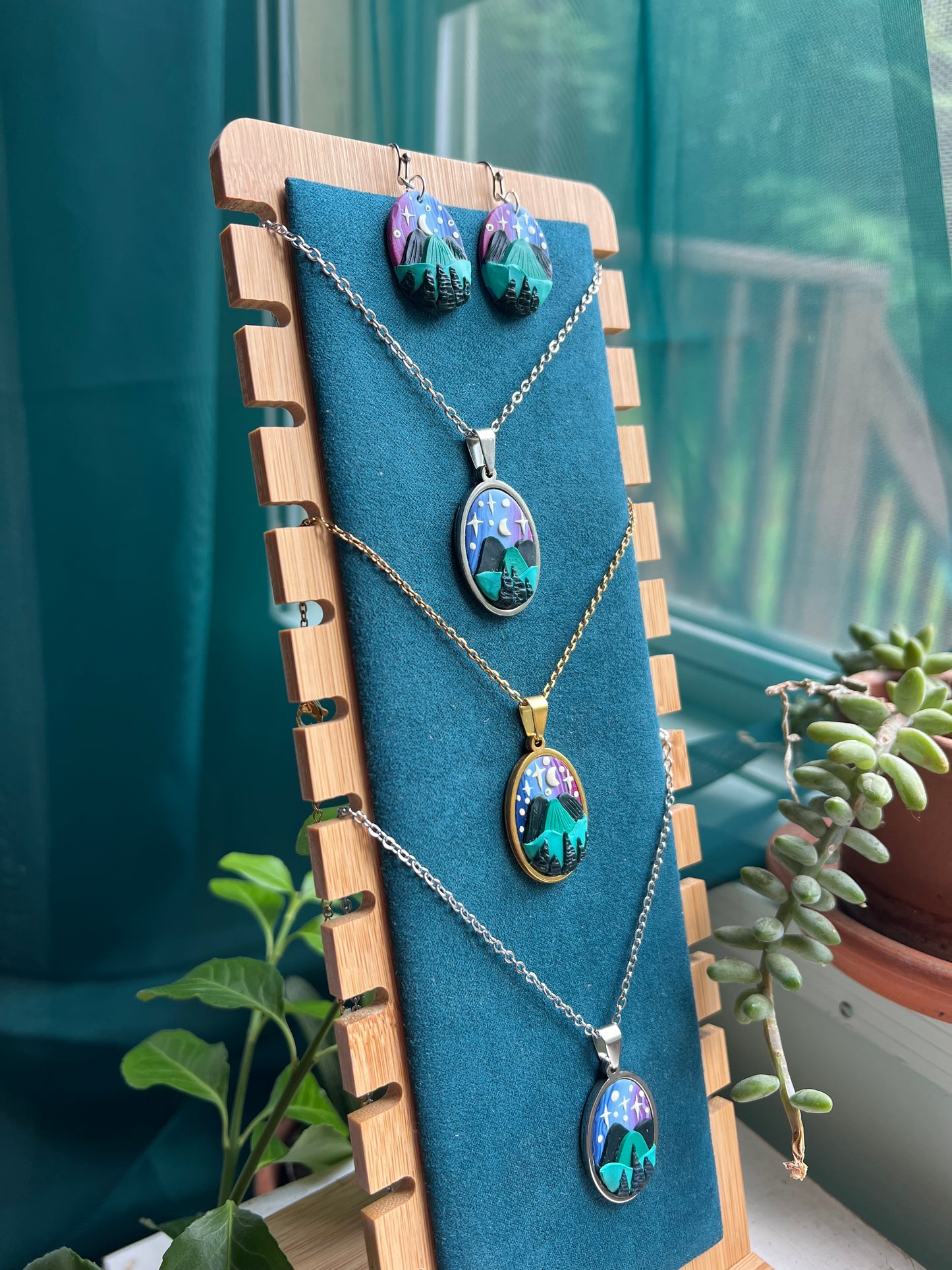Necklaces with colorful pendants on a blue mat with a wooden border, set against a blurred indoor background.