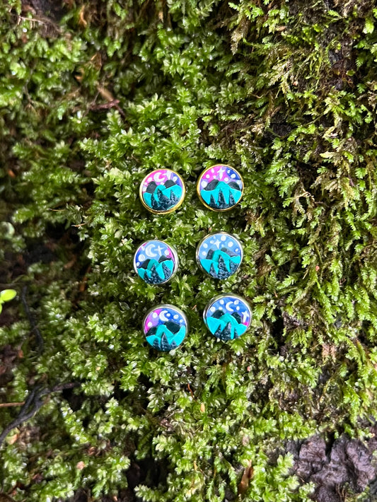 Starry mountain scene stud earrings on mossy stone background