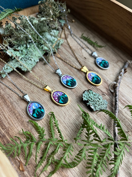 Necklaces with nature-themed starry mountain pendants on a wooden surface with moss and leaves.