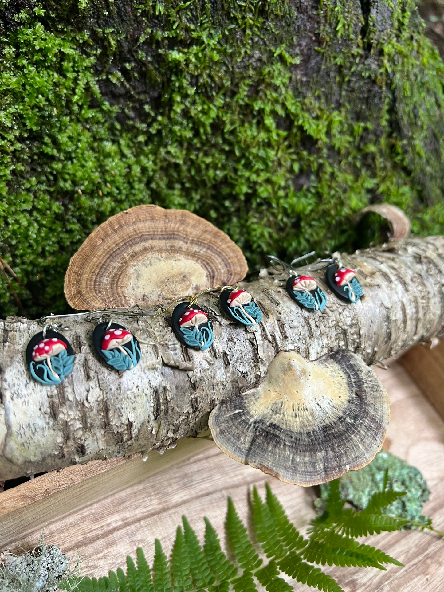 Mushroom Earrings on a tree branch with mushrooms and greenery.