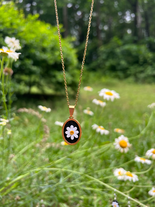 Necklace with a pendant featuring a daisy design against a natural background with flowers.