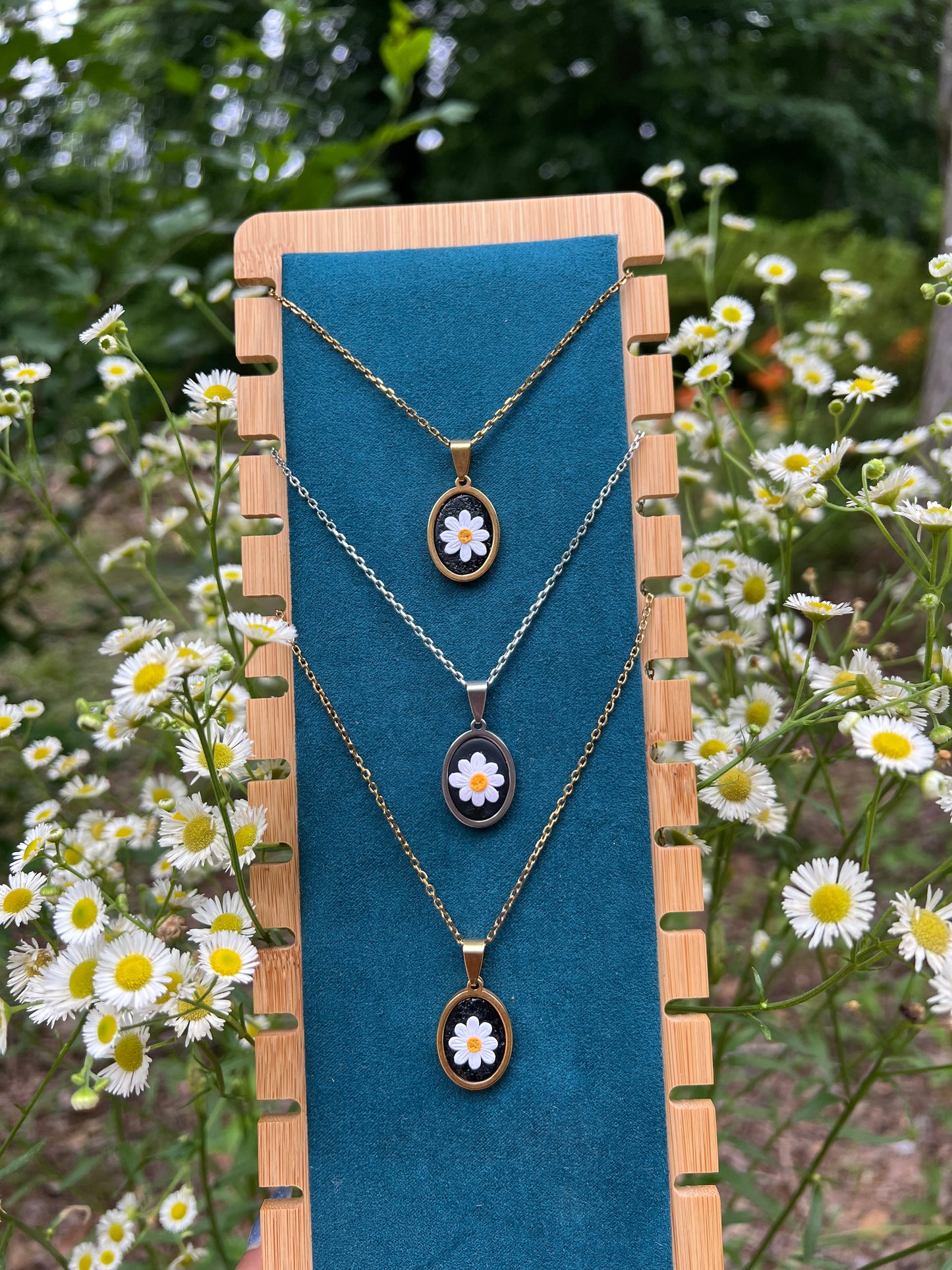 Necklace with daisy pendants on a blue stand with floral background