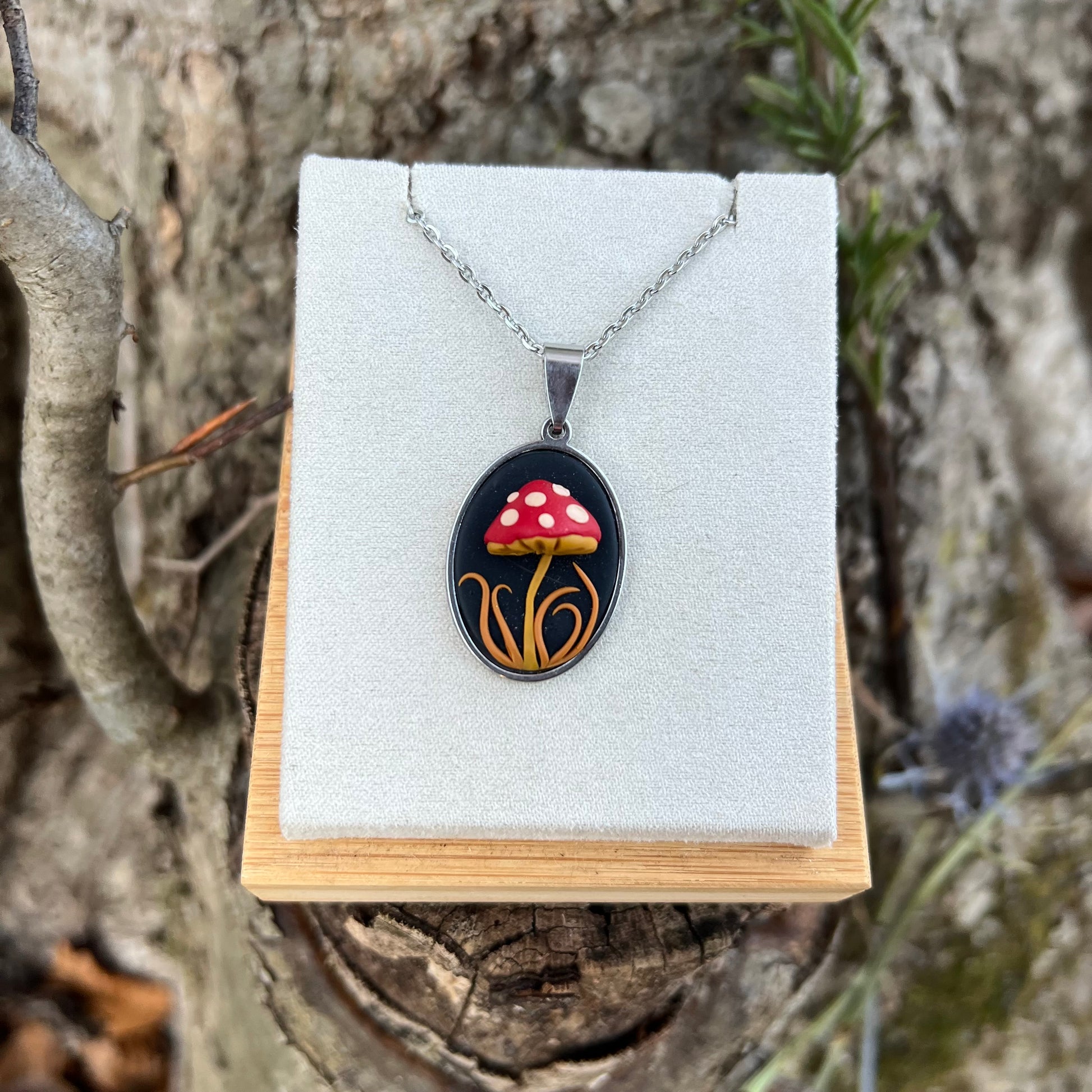 Hand-scuplted polymer clay Mushroom pendant necklace on a display stand with a natural background