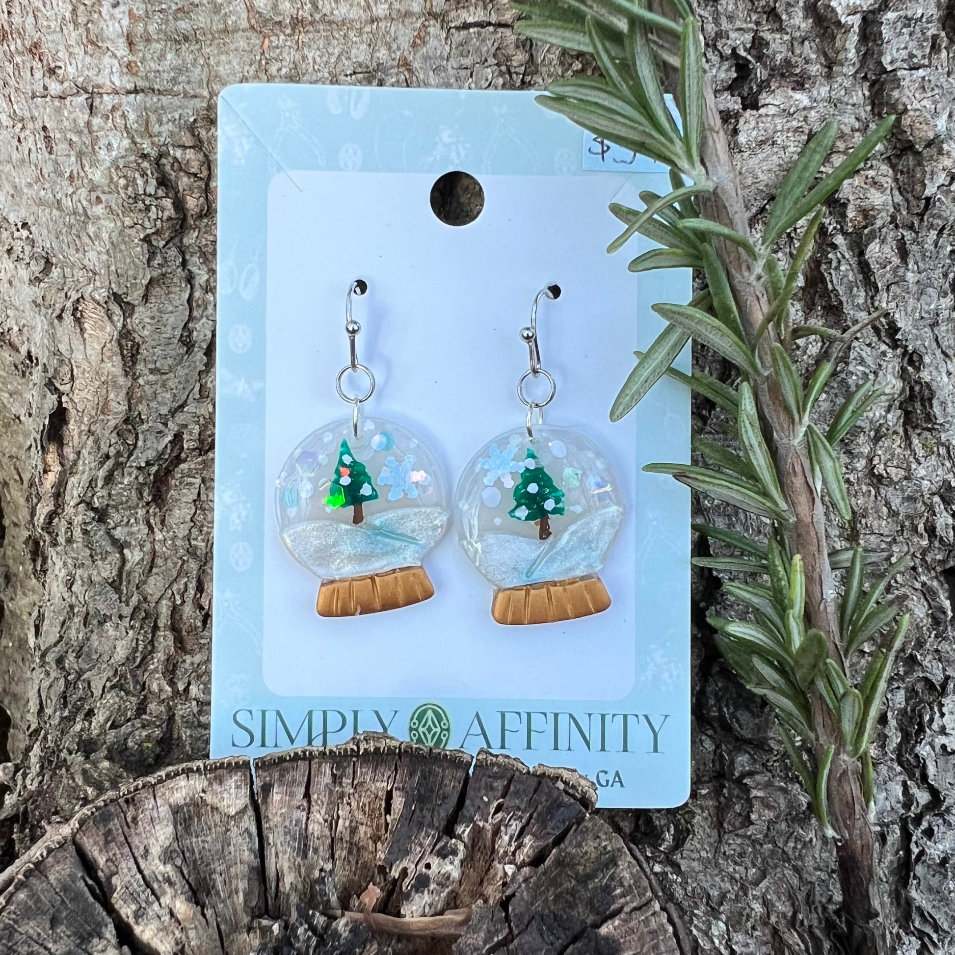 Snowglobe Earrings in a 'Simply Affinity' packaging on a wooden surface with a plant.