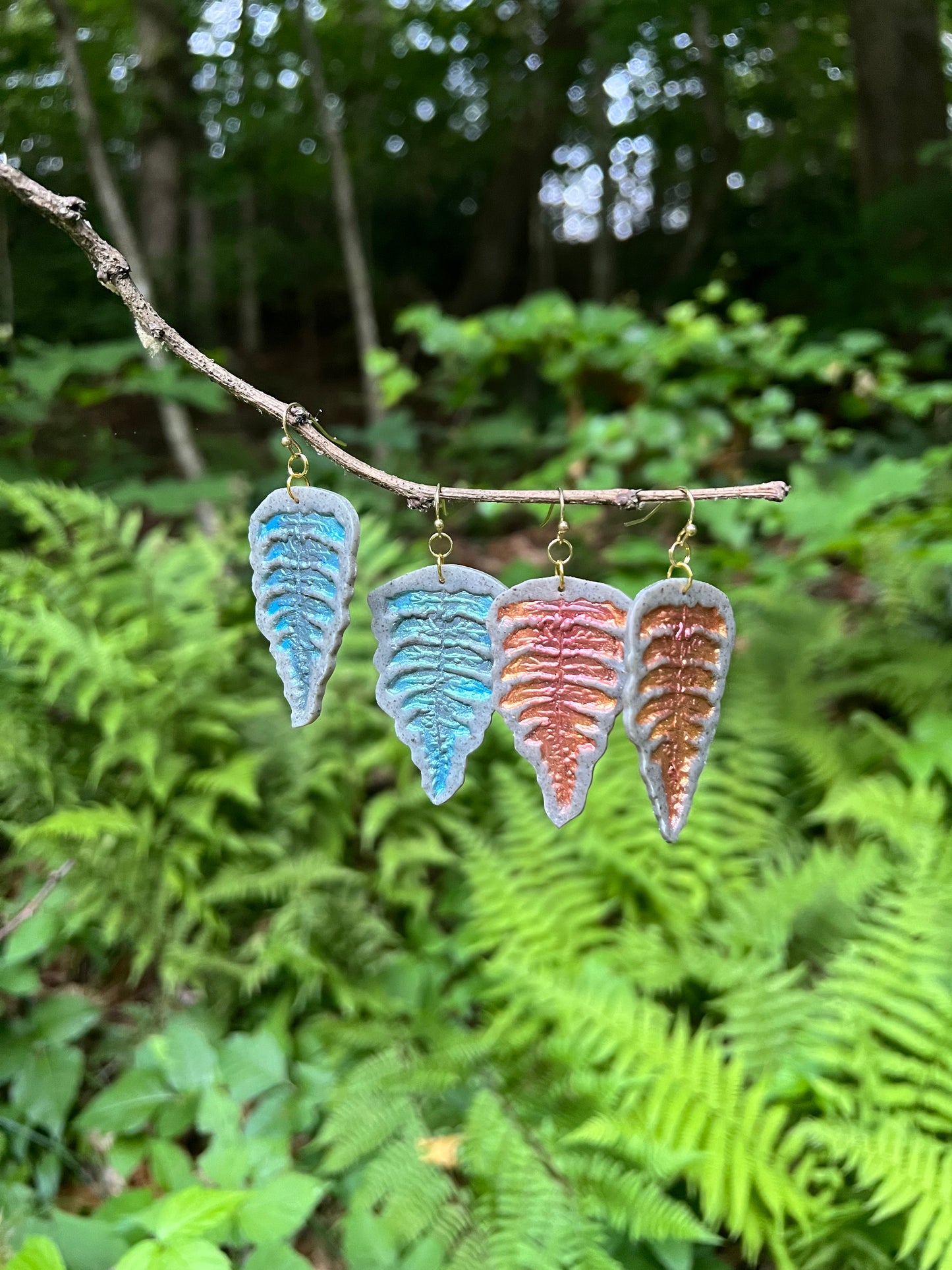 Fern-shaped polymer clay earrings on a branch with a natural background