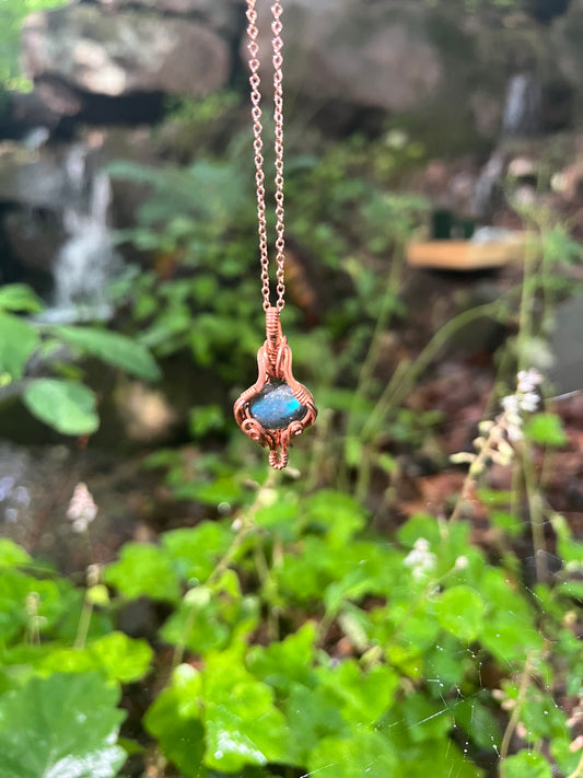 Labradorite wire wrapped pendant in front of a waterfall and foam flowers