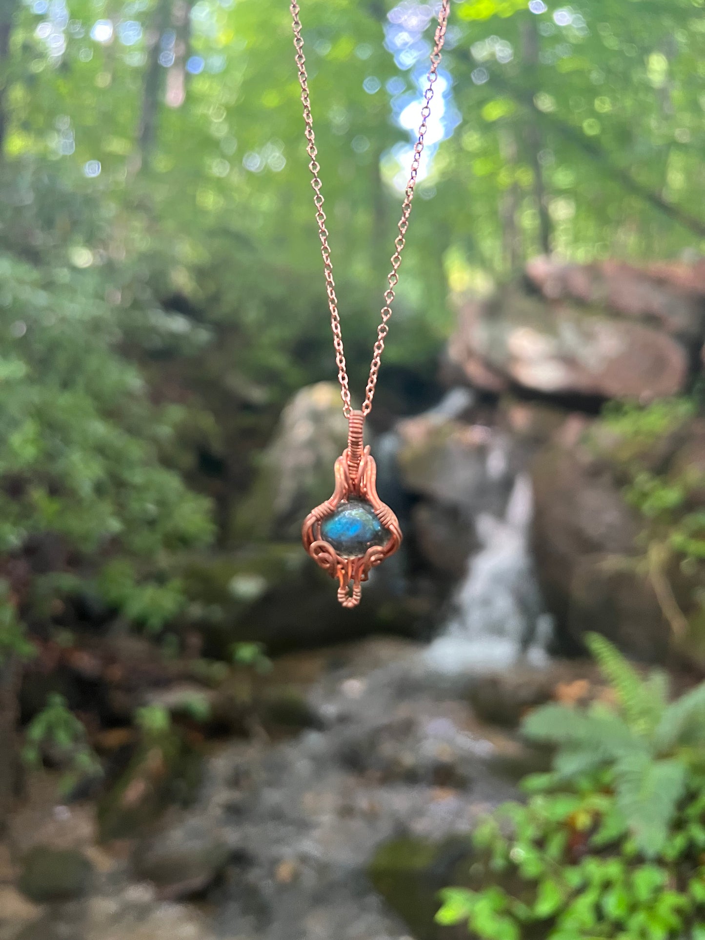 labradorite and copper wire wrapped pendant in front of waterfall 