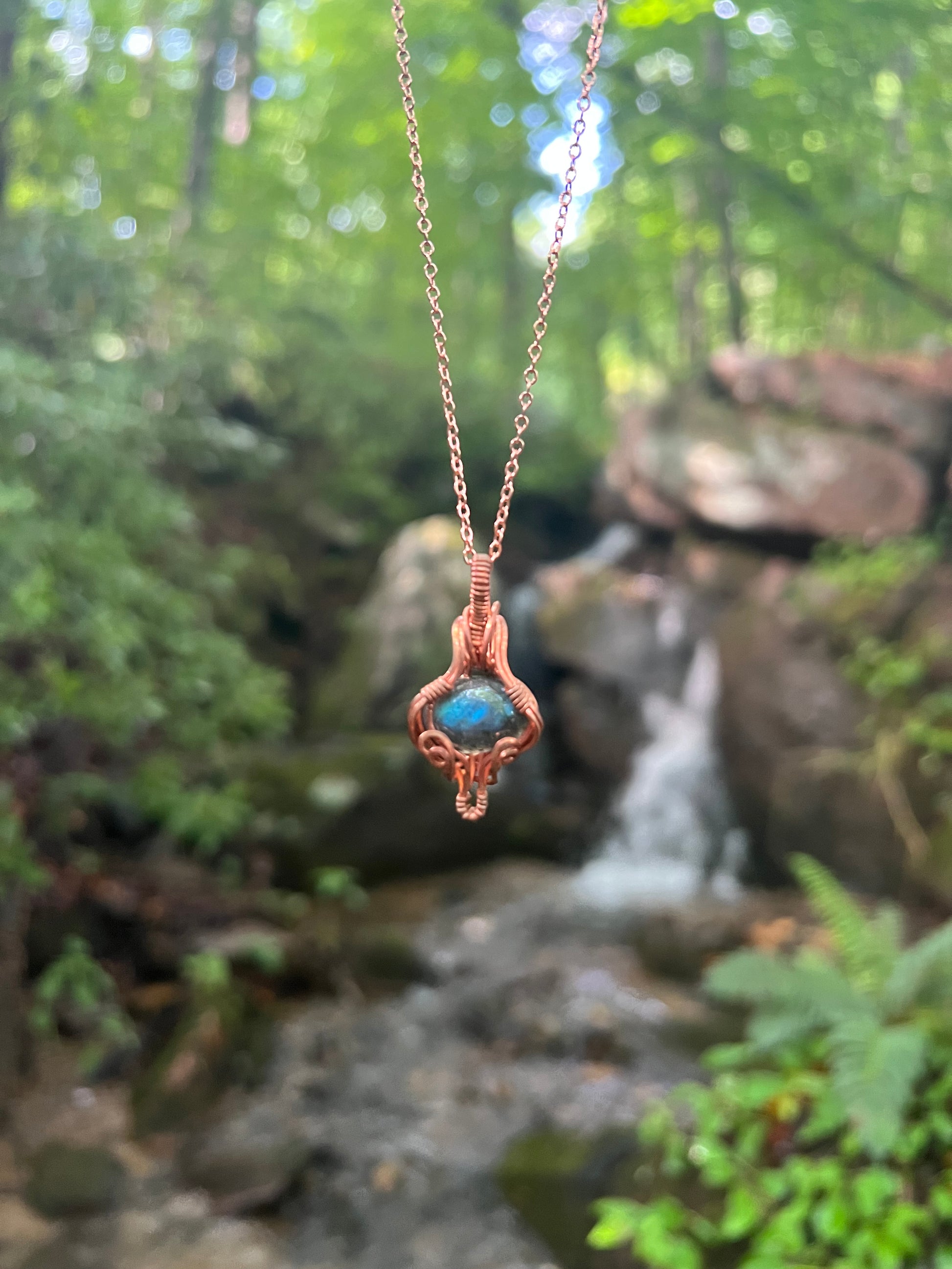 labradorite and copper wire wrapped pendant in front of waterfall 