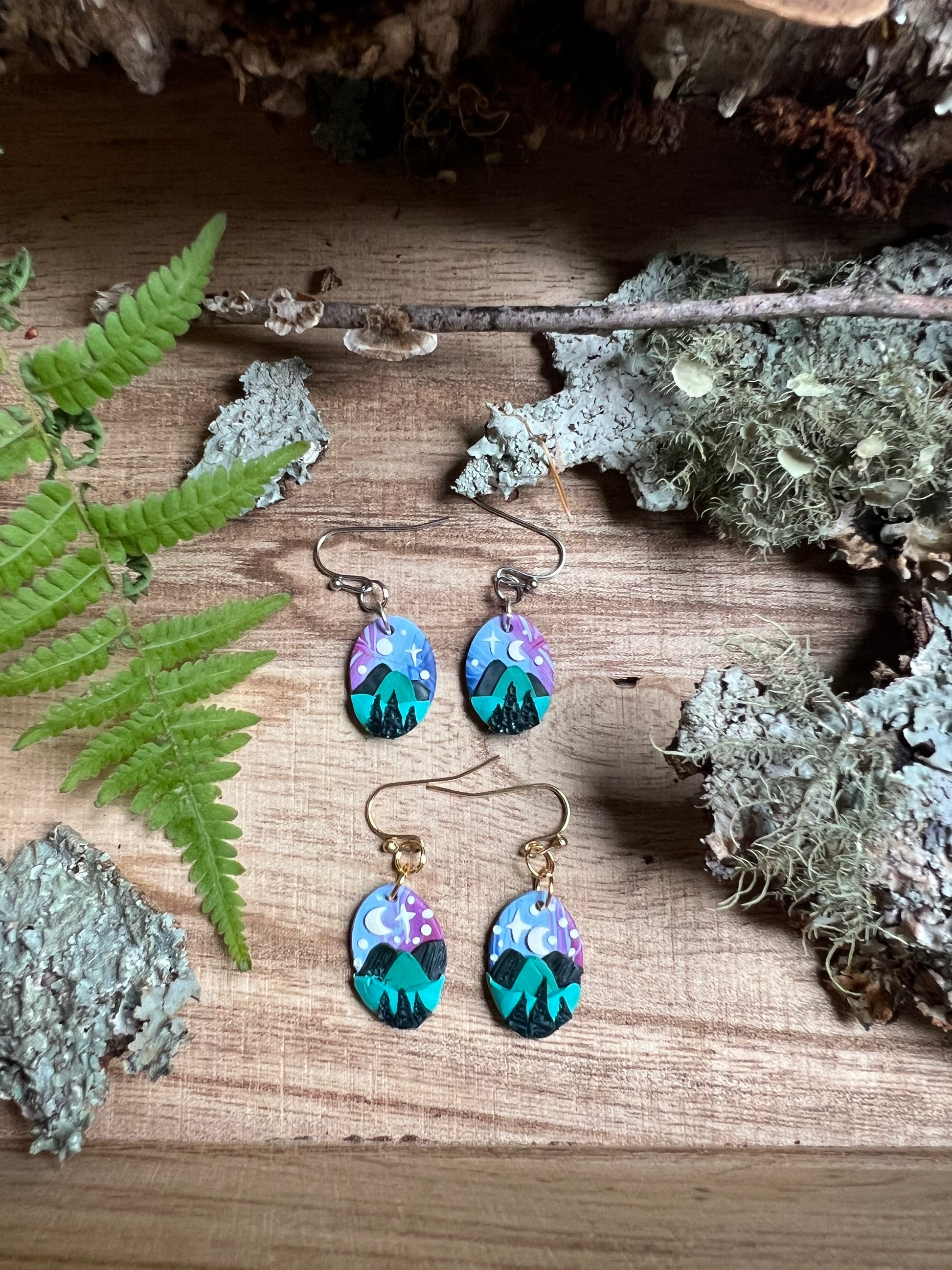 Pair of earrings with nature-themed design on a wooden surface with plants.