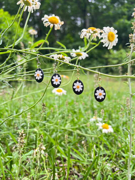 Daisy Polymer clay  earrings hanging from a daisy stem with daisies in the background