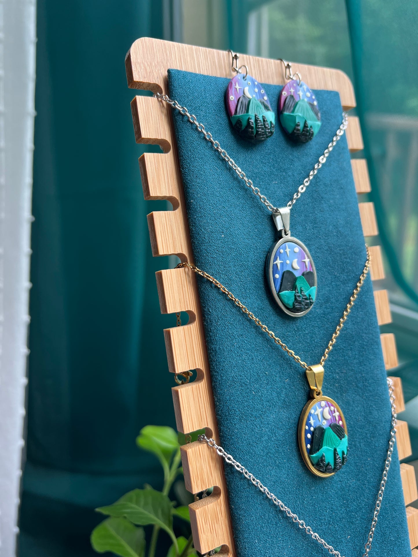 Jewelry set with earrings and a necklace on a wooden stand against a blue background. Hand-sculpted starry blue ridge mountain polymer clay necklace and earring set. 