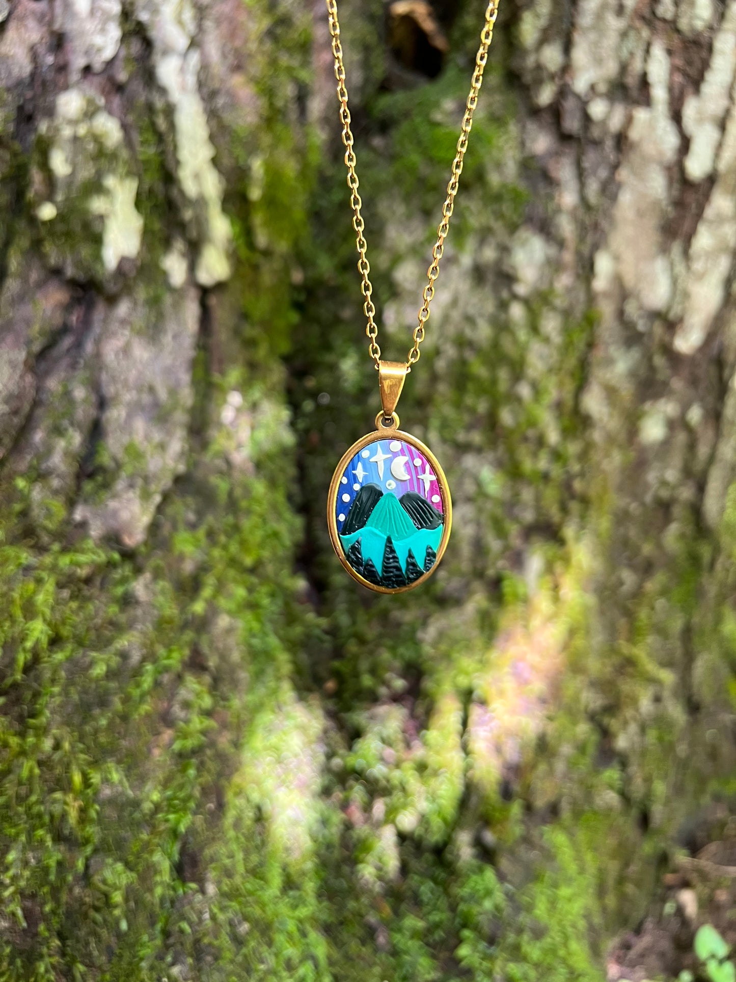 Hand-sculpted starry blue ridge mountain polymer clay necklaces with nature-themed pendants on a mossy surface.