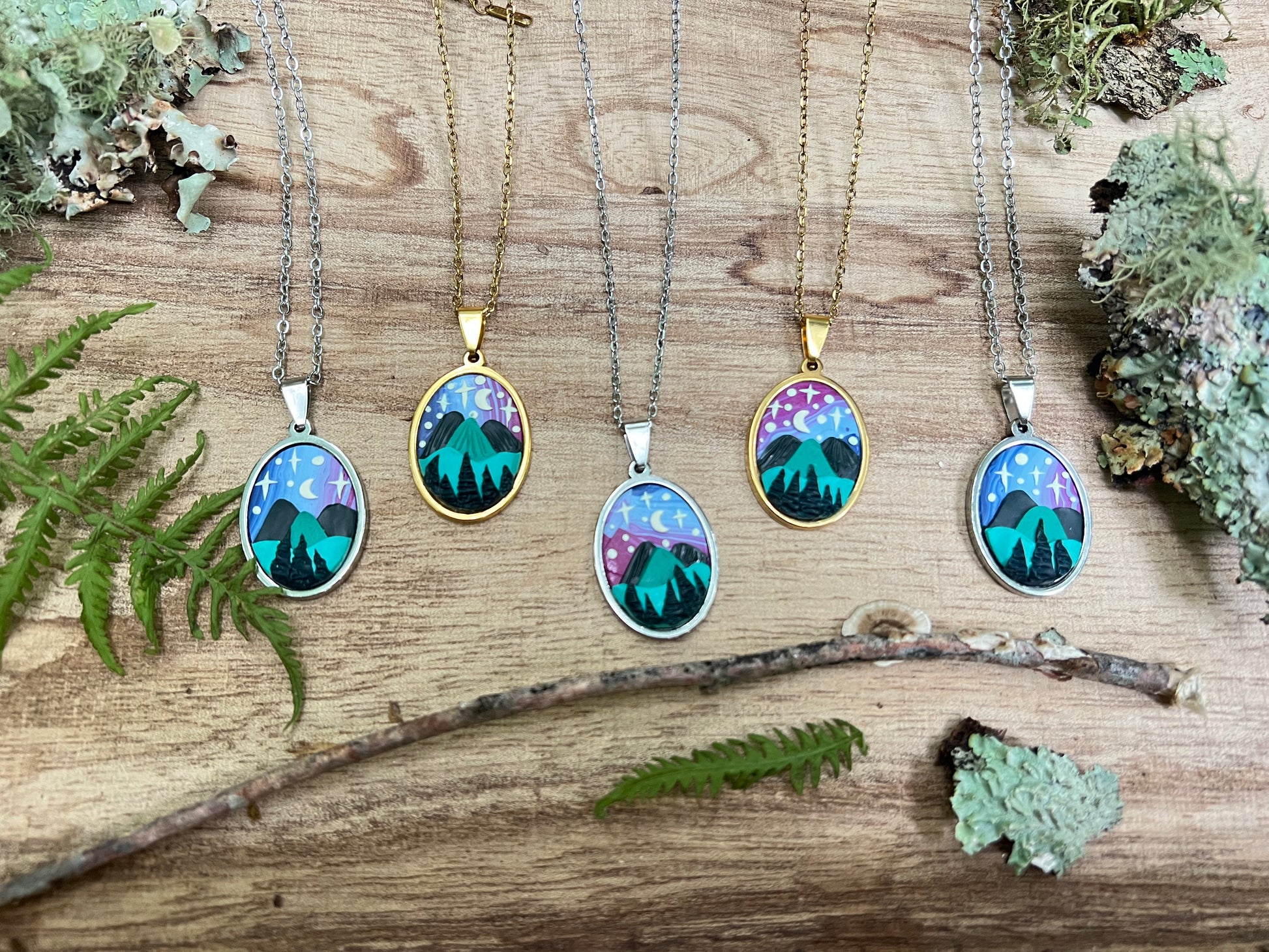 Five necklaces with nature-themed pendants on a wooden surface with greenery.