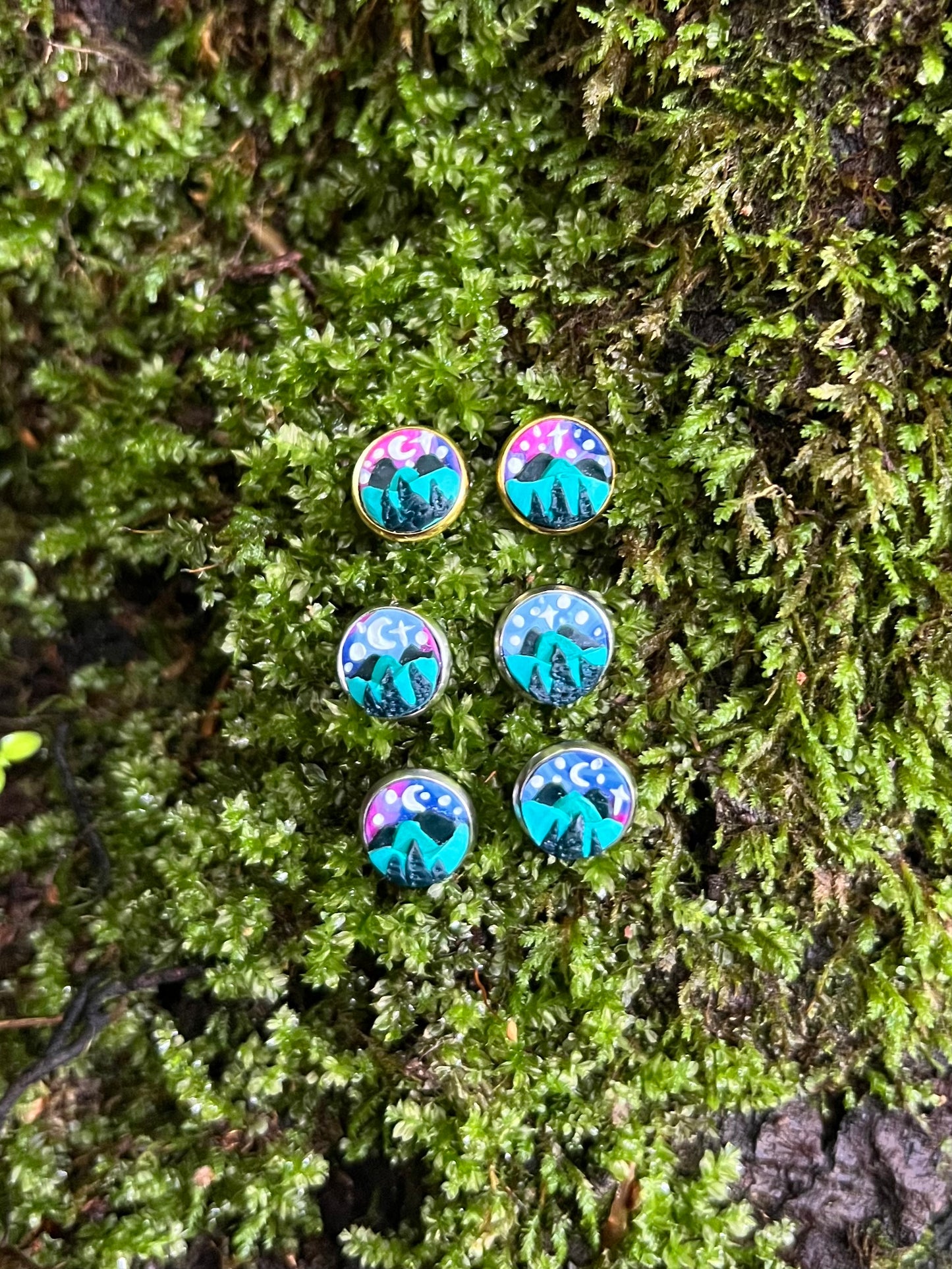 Starry mountain scene stud earrings on mossy stone background