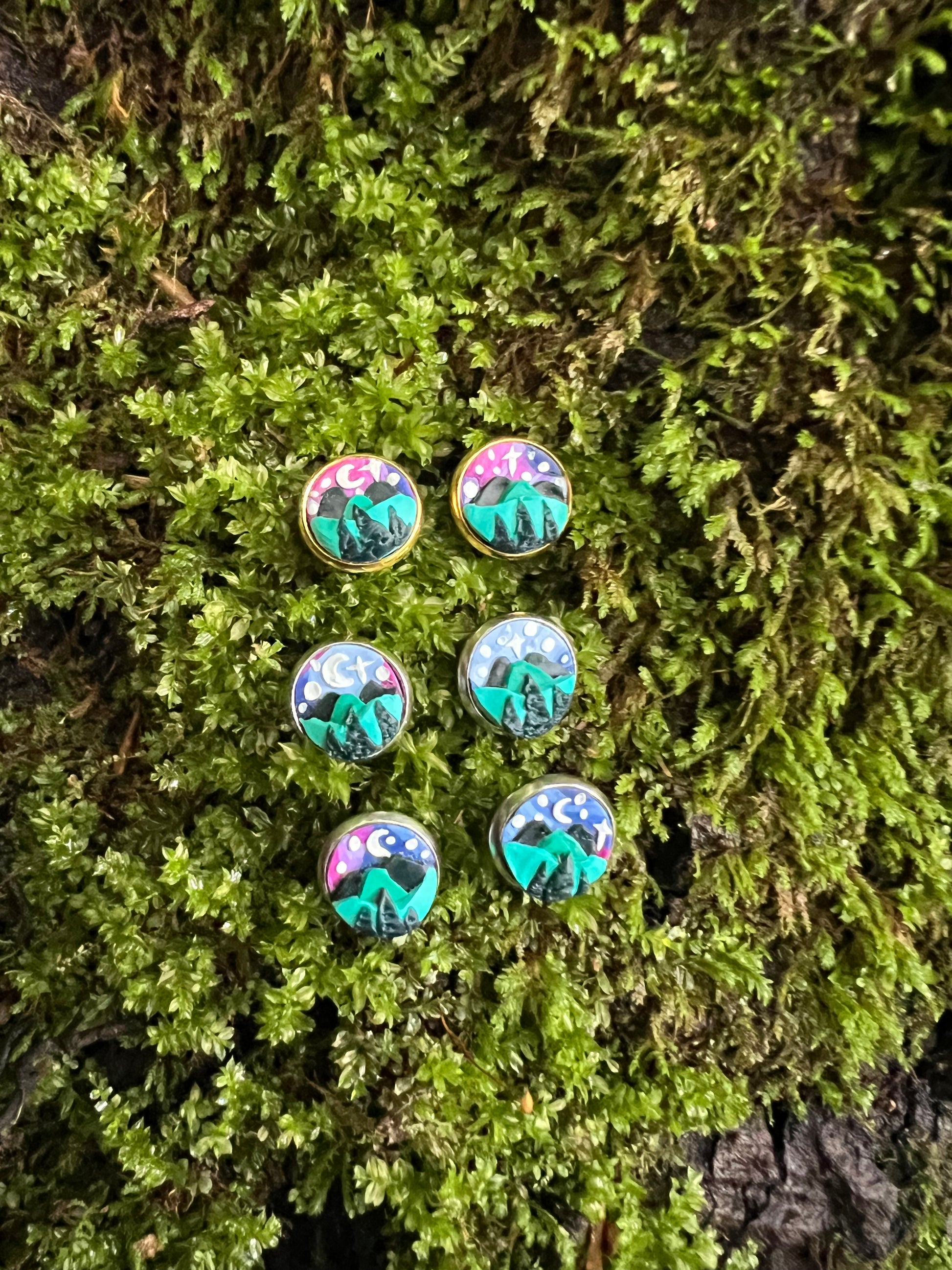 Starry mountain scene stud earrings on mossy stone background