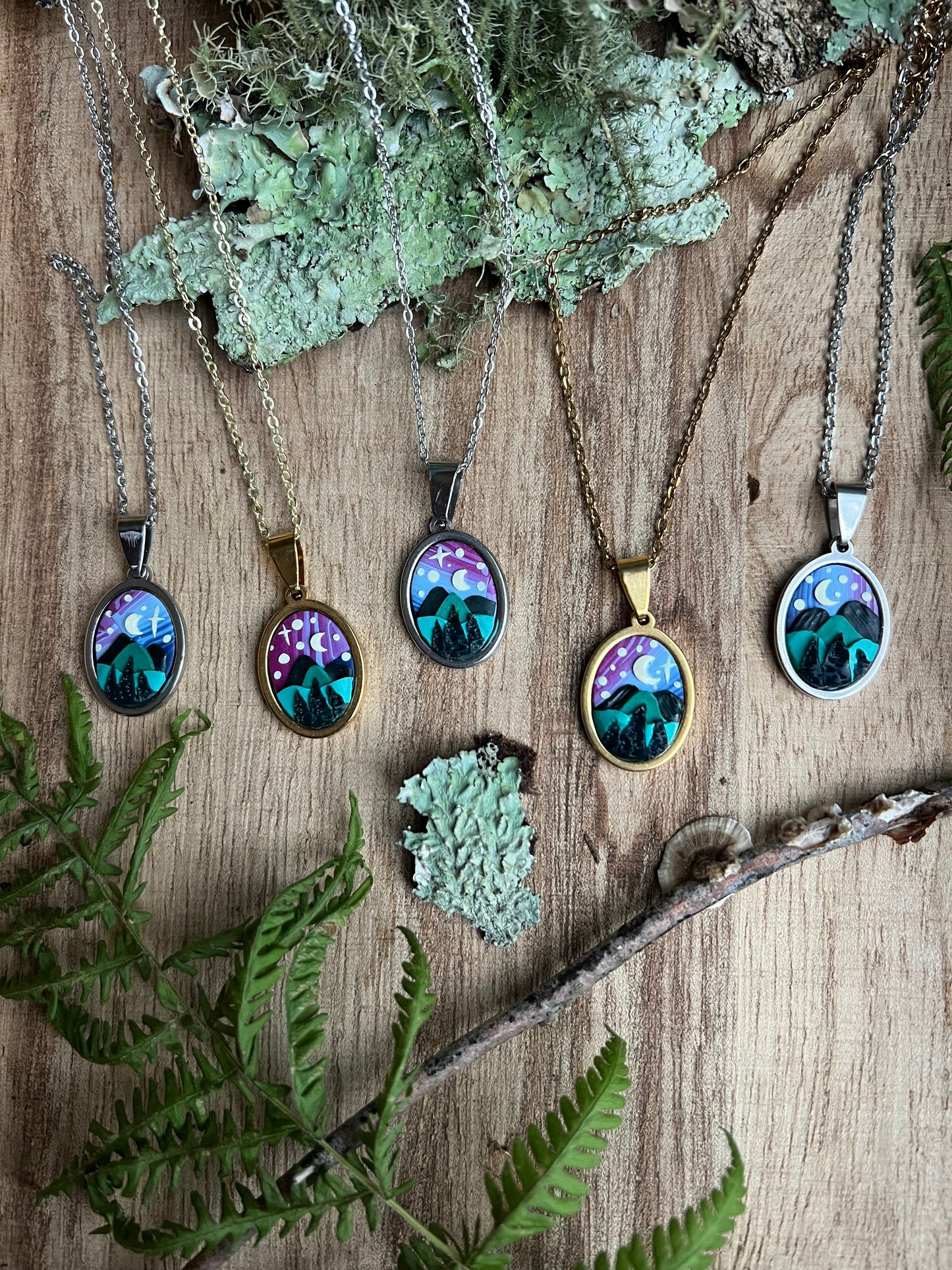 Five necklaces with nature-themed pendants on a wooden surface with greenery.
