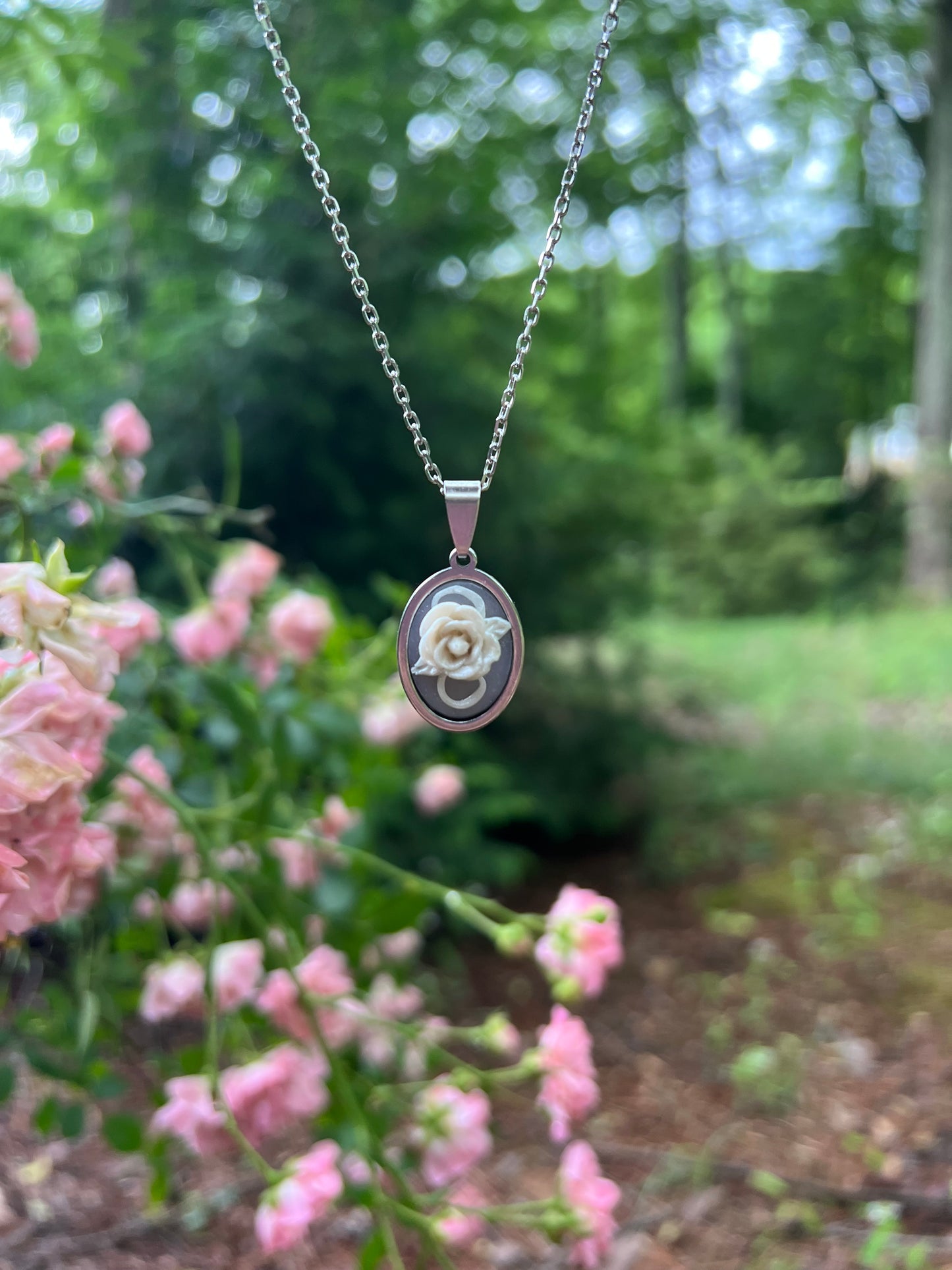 Hand sculpted white rose polymer clay necklace with pink roses in the background 