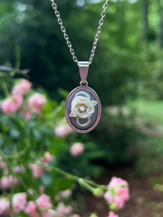 Hand sculpted white rose polymer clay necklace with pink roses in the background 