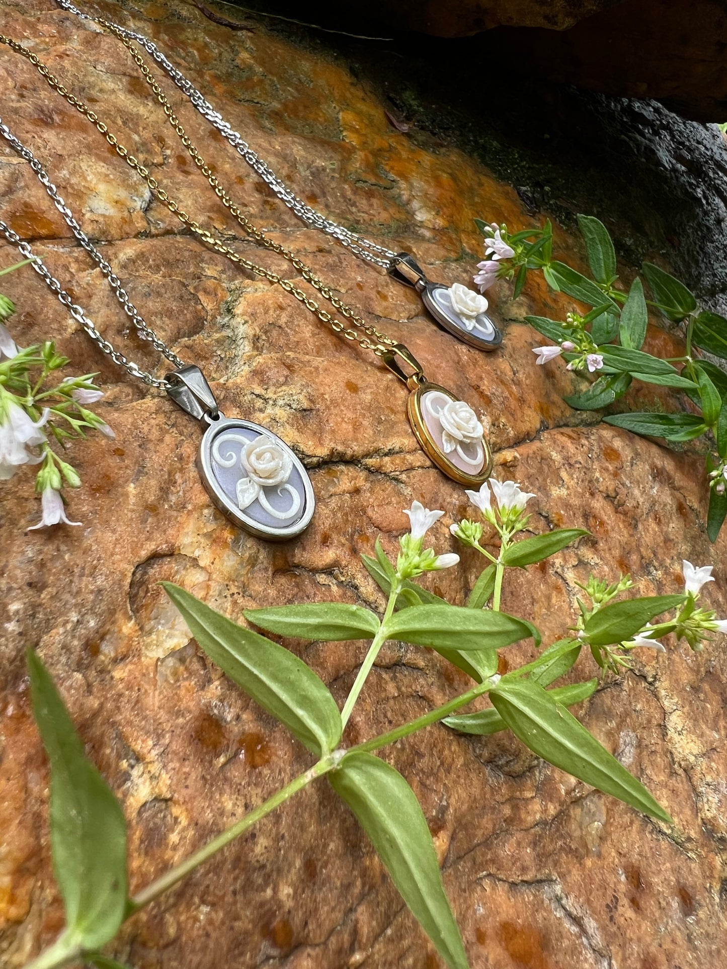 Three necklaces with pendants on a textured stone surface with green leaves and flowers.