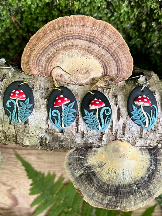 Set of hand sculpted mushroom earrings on a natural background with tree bark and ferns.