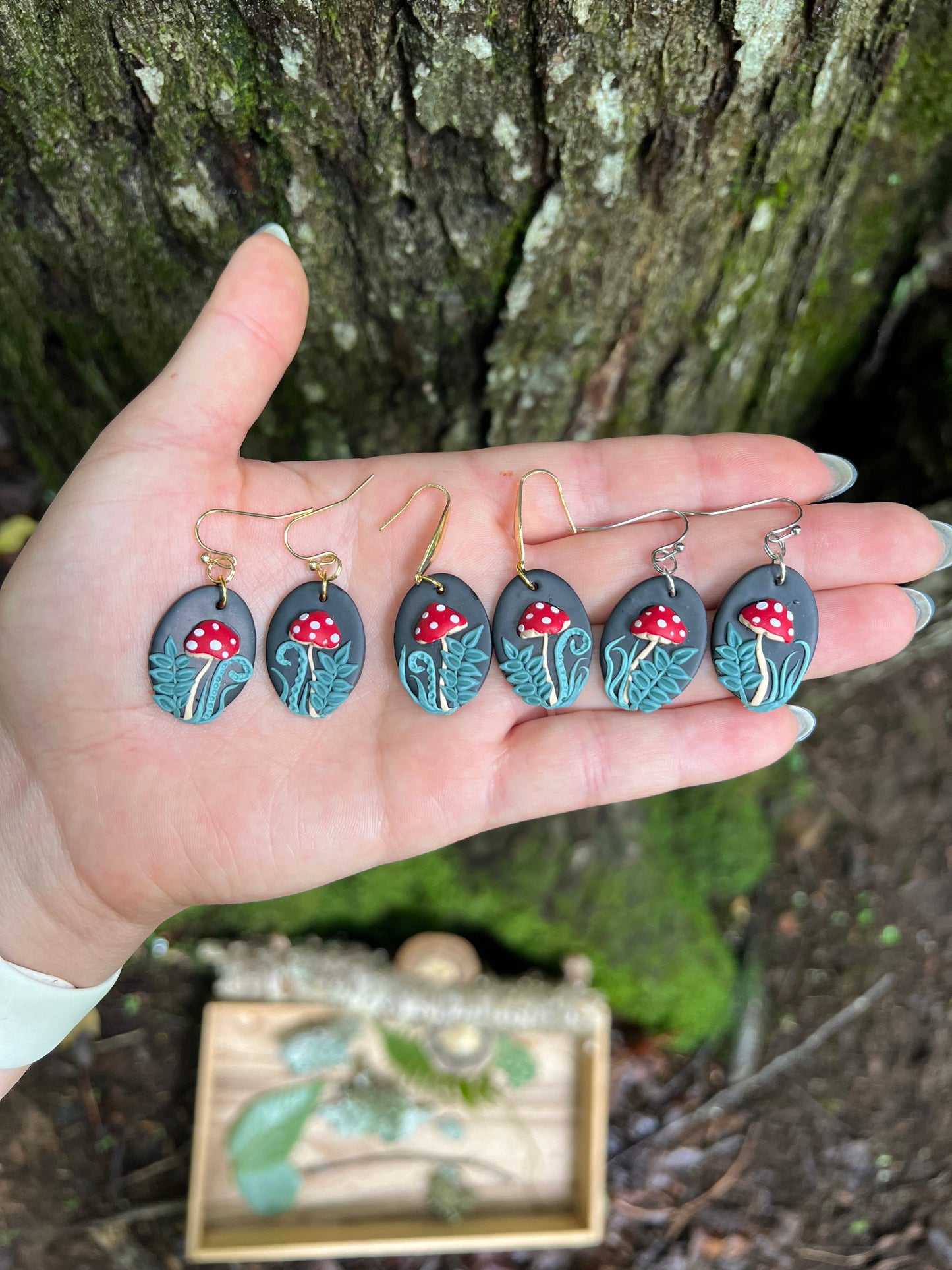 Hand holding polymer clay mushroom earrings against a natural background