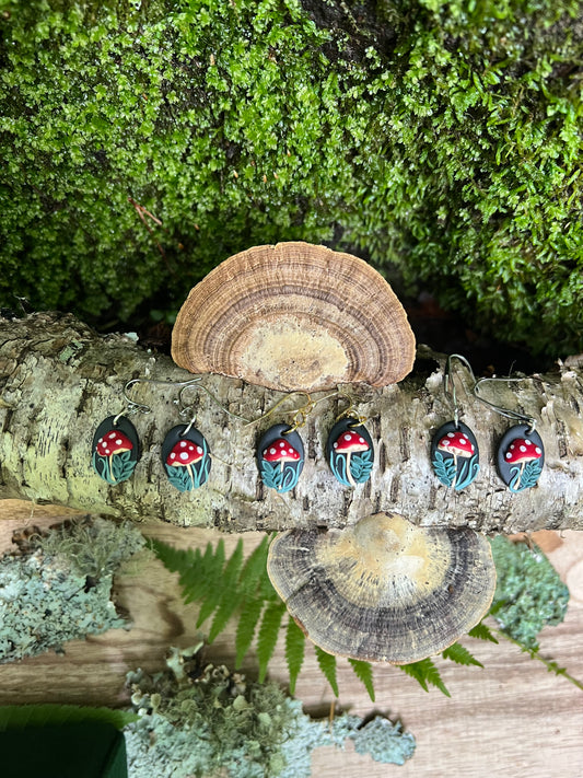 Polymer Clay Mushroom earrings on a tree trunk with mushrooms and greenery.