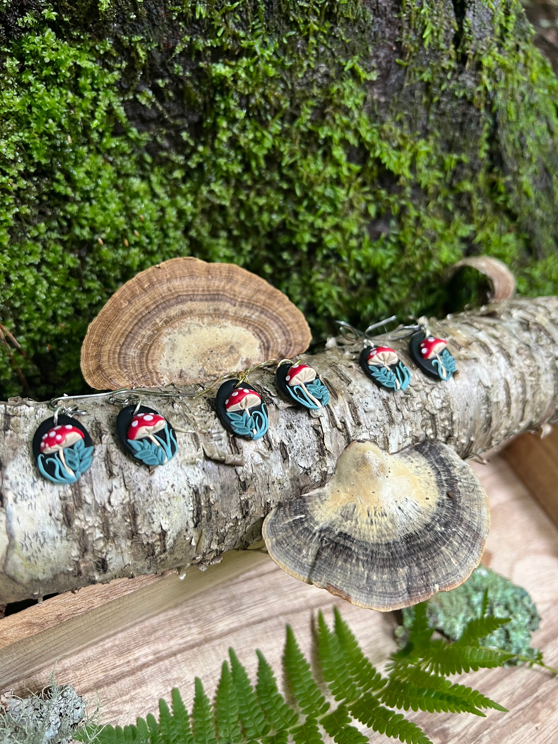 Mushroom Earrings on a tree branch with mushrooms and greenery.
