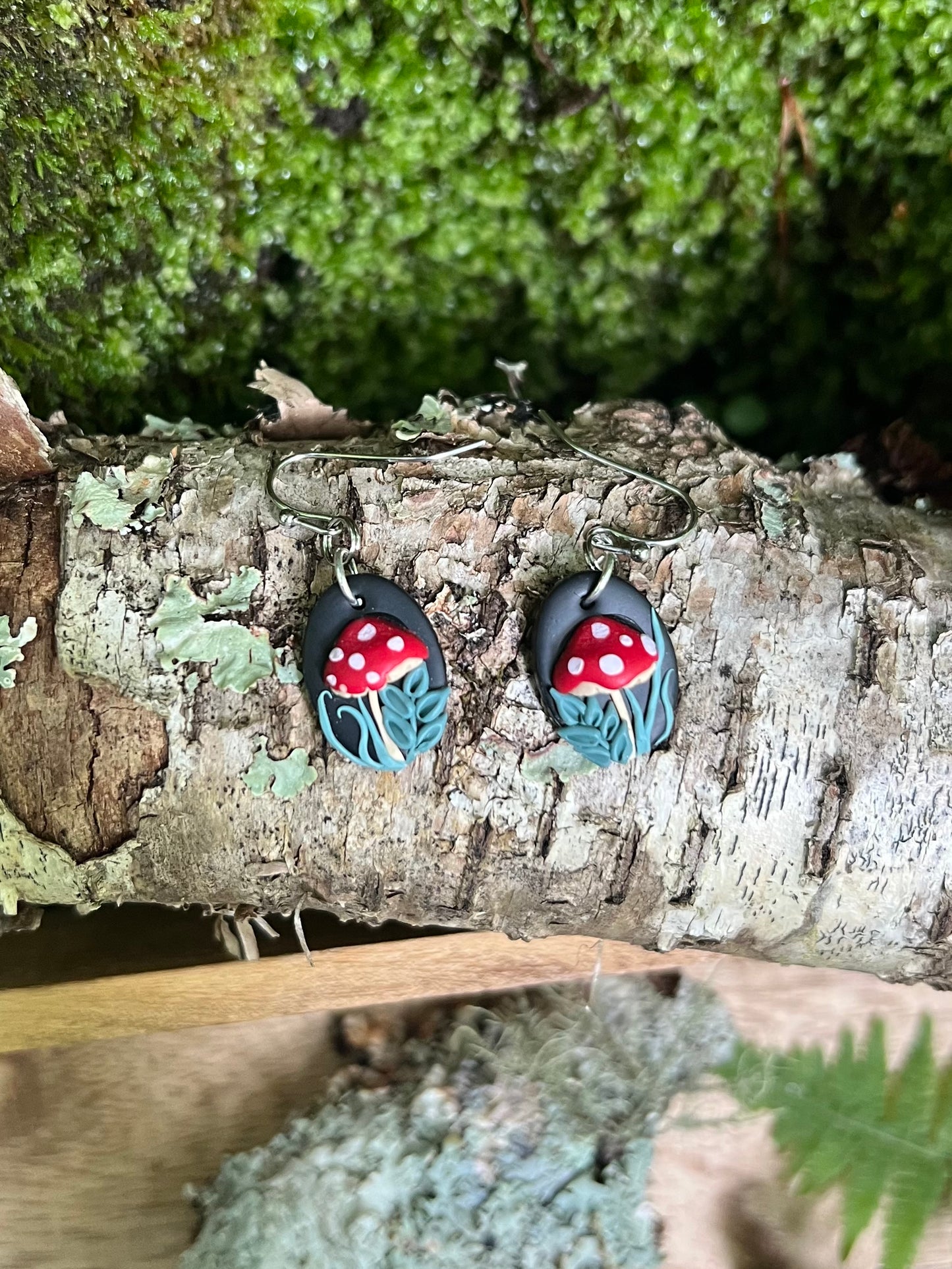 Pair of earrings with red mushroom design on a wooden surface with greenery