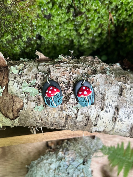 Pair of earrings with red mushroom design on a wooden surface with greenery