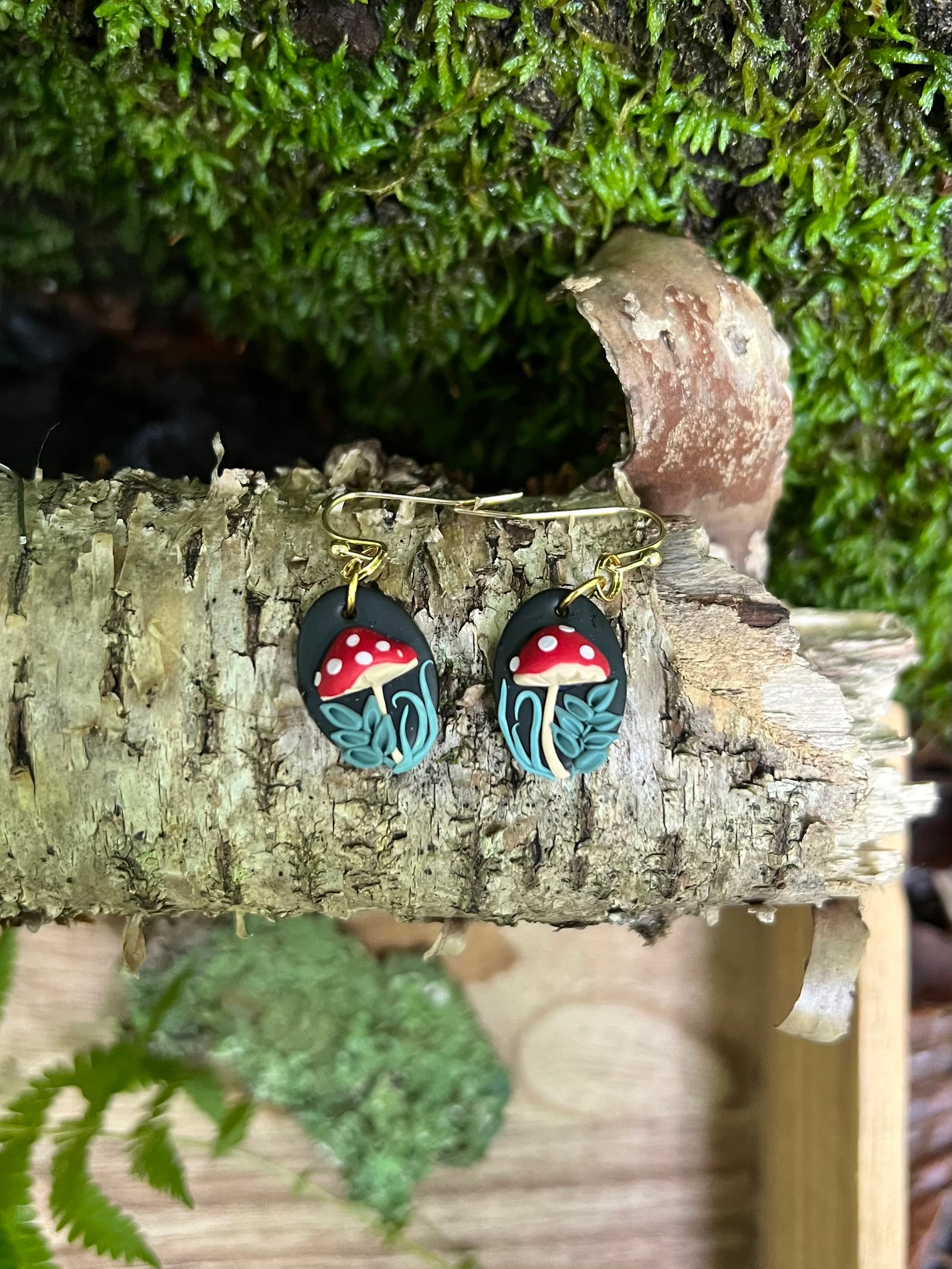 Pair of earrings with mushroom design on a wooden surface with greenery