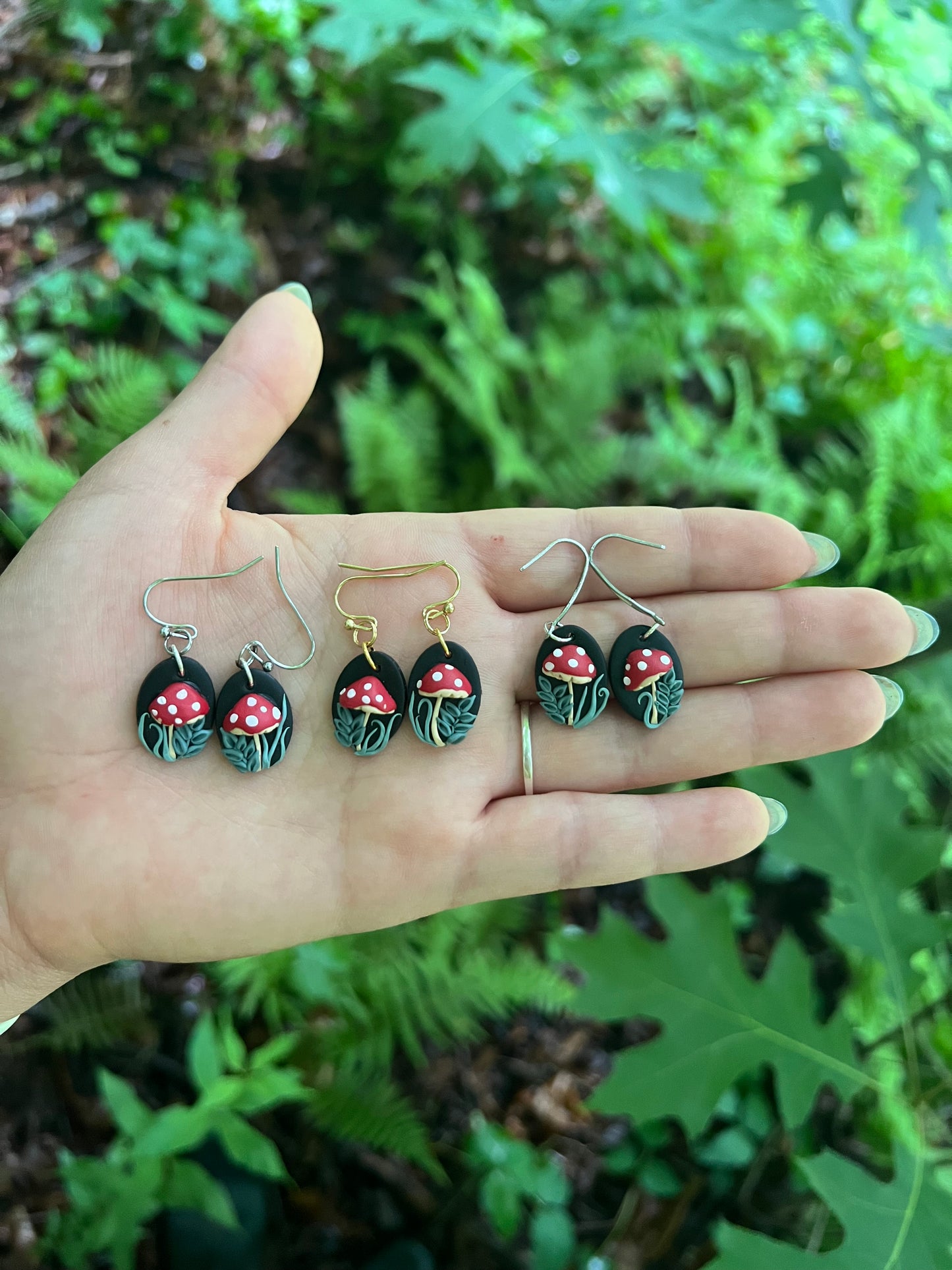 Hand holding mushroom earrings with a forest background