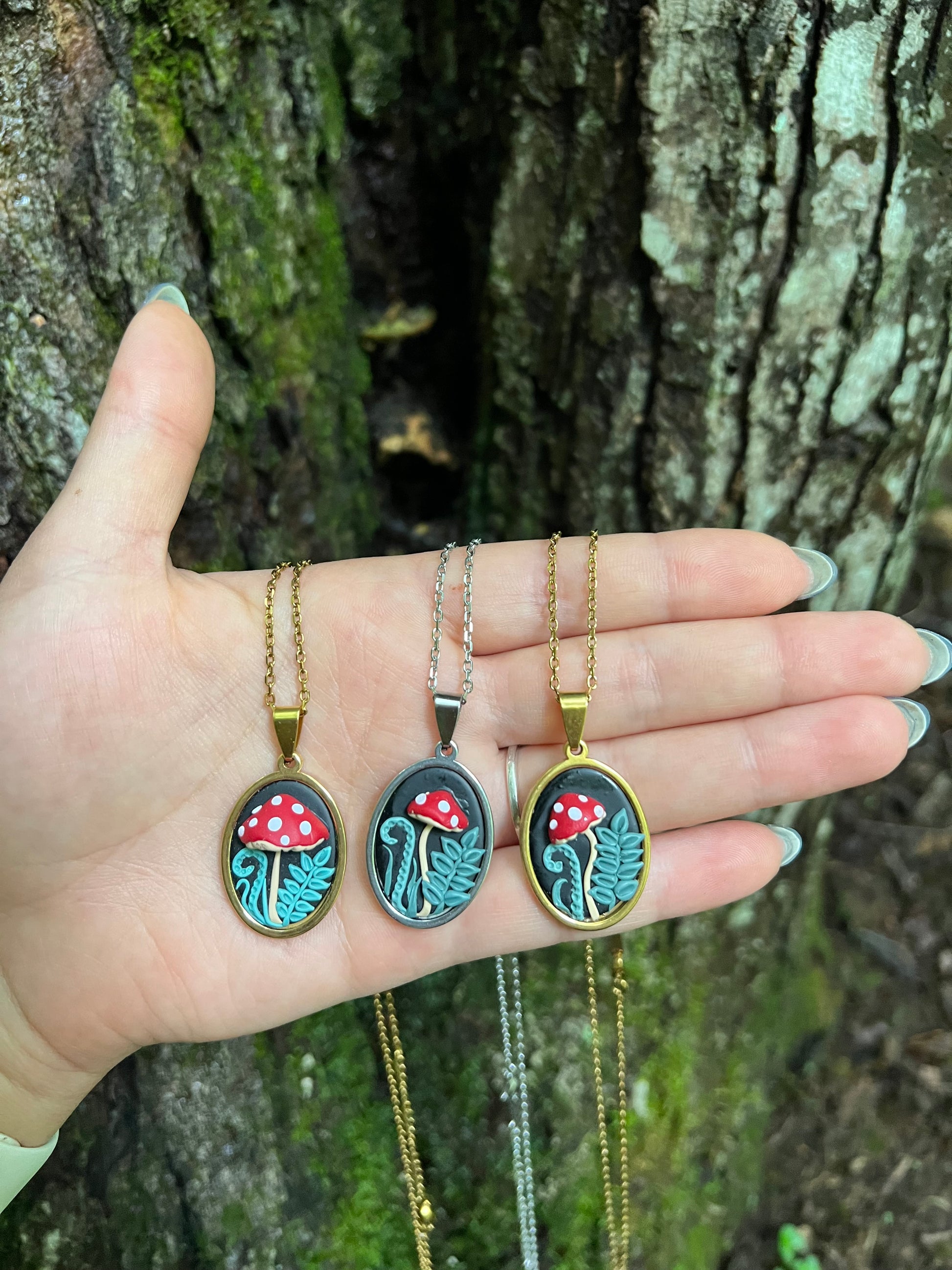 Hand holding three mushroom necklaces with pendant designs against a natural background