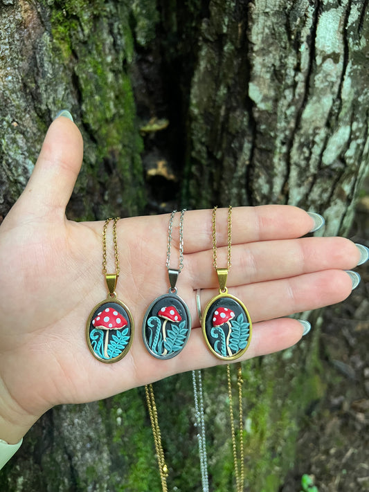 Hand holding three mushroom necklaces with pendant designs against a natural background
