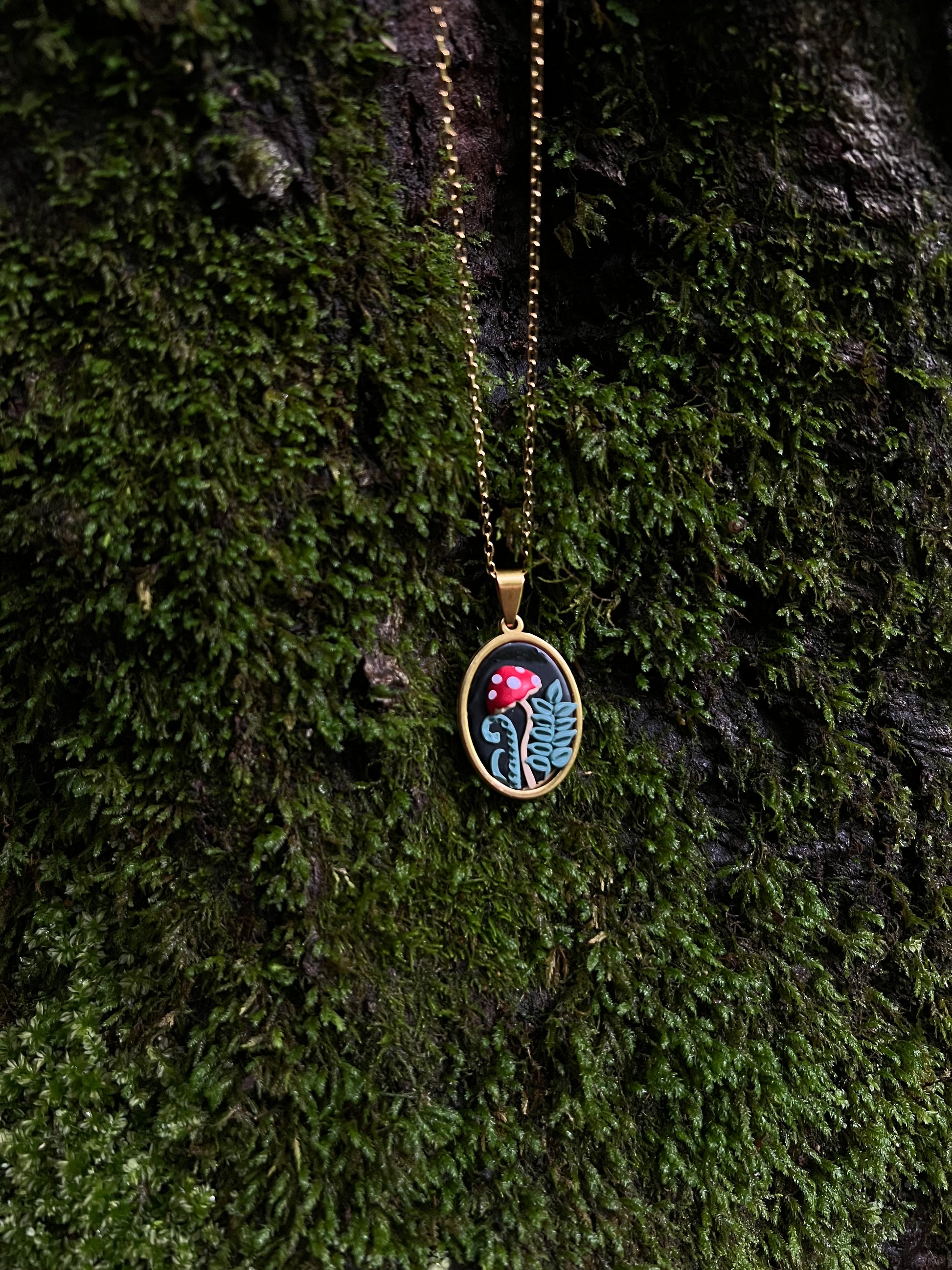 Gold mushroom necklace with a pendant on a mossy surface