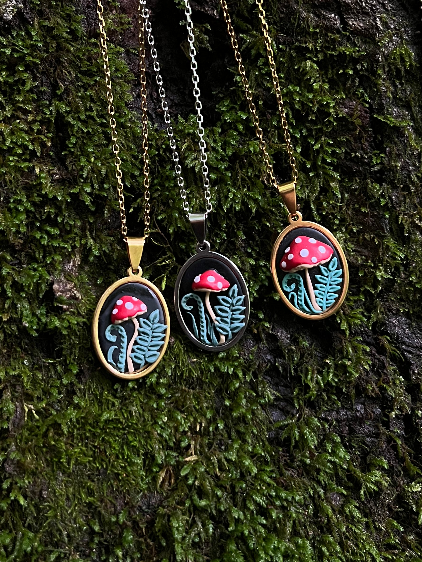 Three mushroom-themed necklaces on a mossy tree bark background