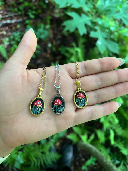 Three mushroom-themed necklaces on a hand with a green leafy background