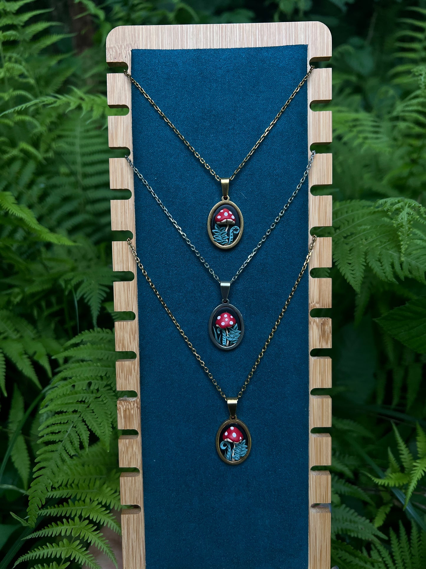 Three necklaces with mushroom pendants on a blue card against a green fern background