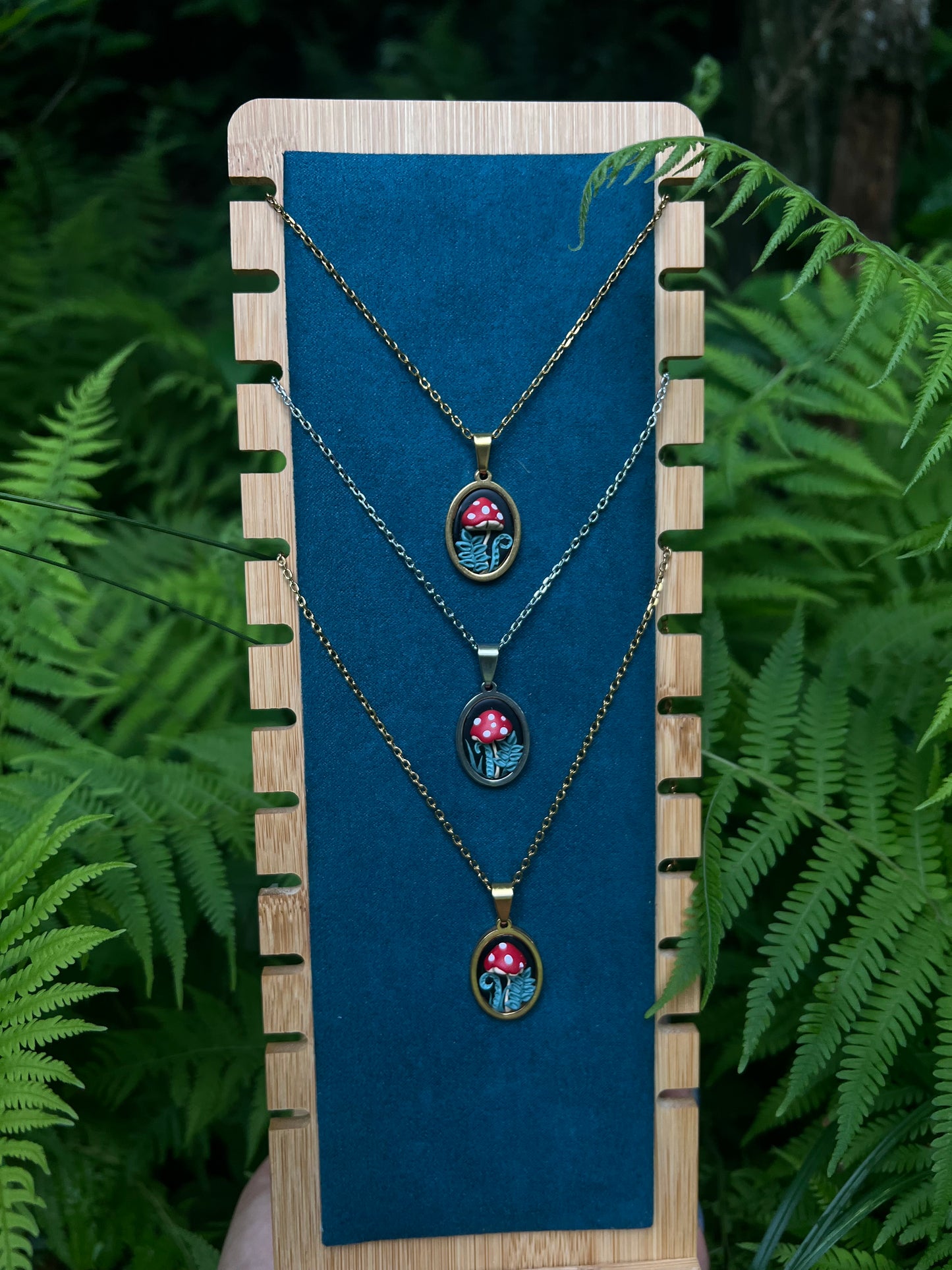 Necklace with mushrooms and fern pendants on a blue stand against a green fern background