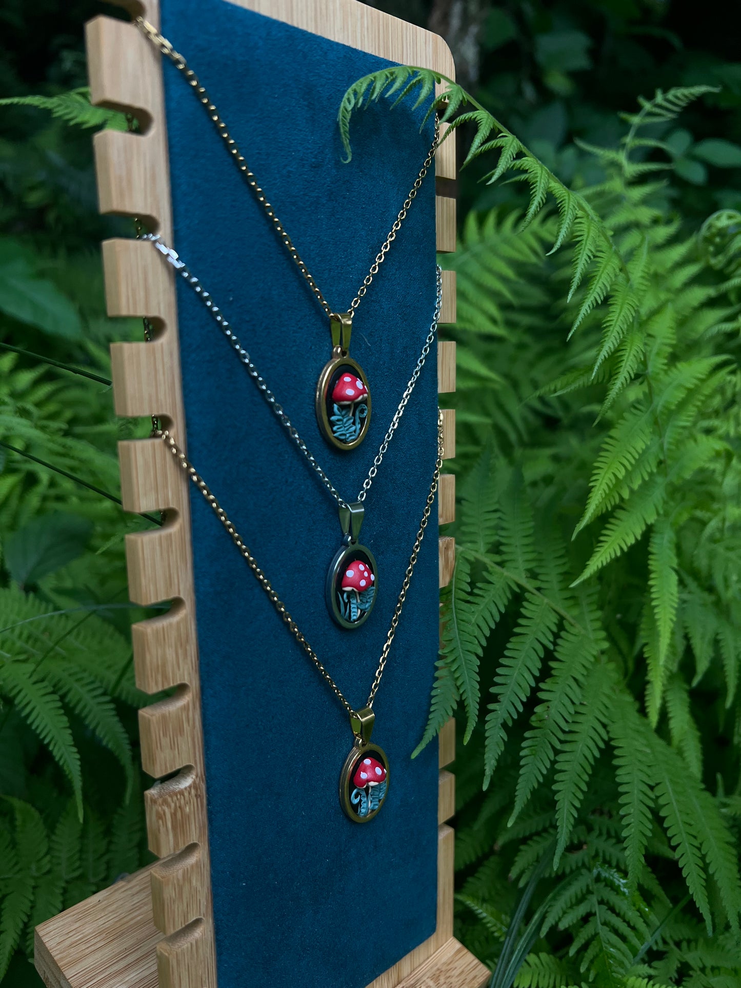 Necklace with hand sculpted mushrooms out of polymer clay on a stand with ferns in the background