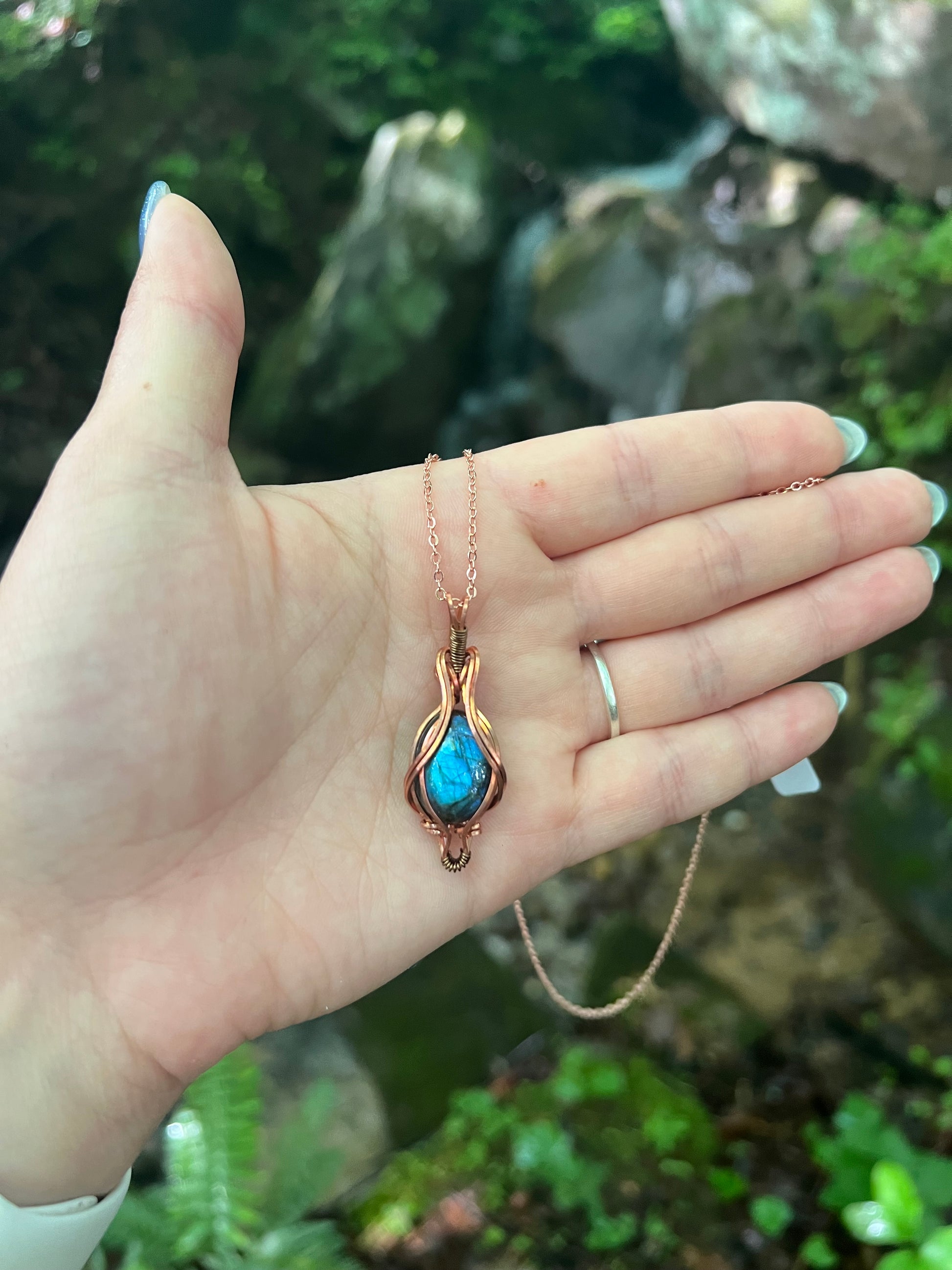 Hand holding a necklace with a blue labradorite pendant against a natural background