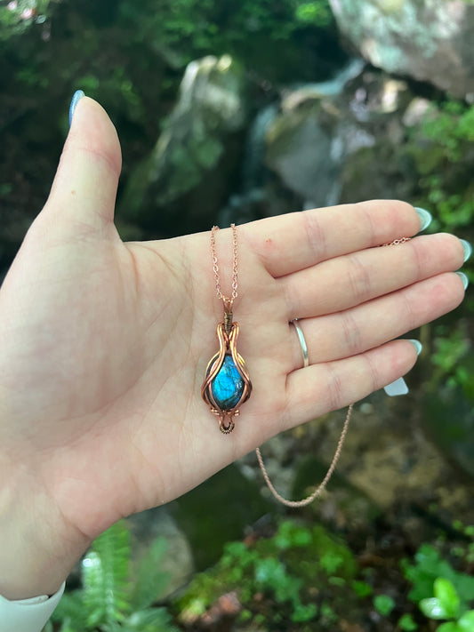 Hand holding a necklace with a blue labradorite pendant against a natural background