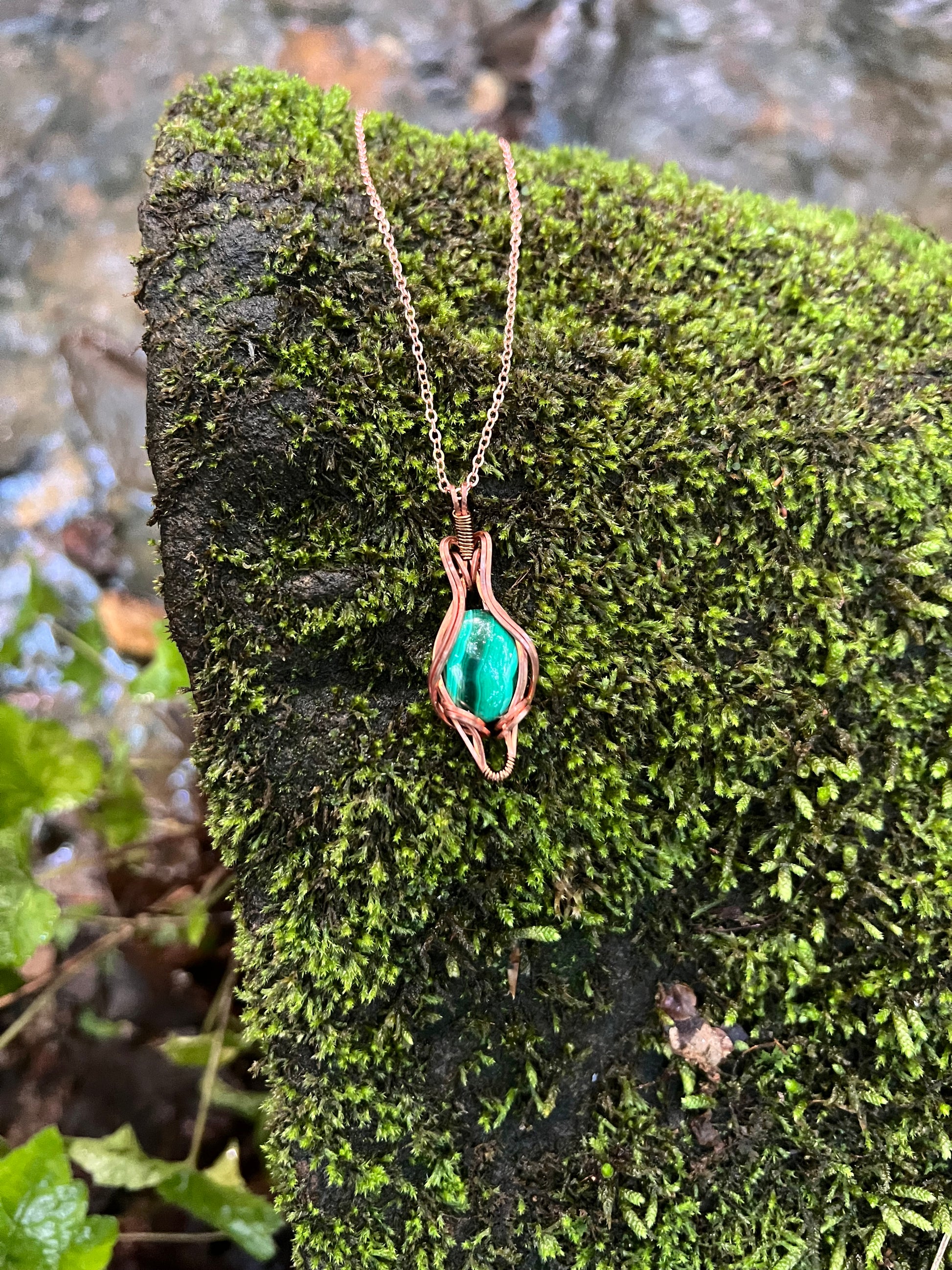 Wire Wrapped Malachite and Copper Necklace against a mossy stone