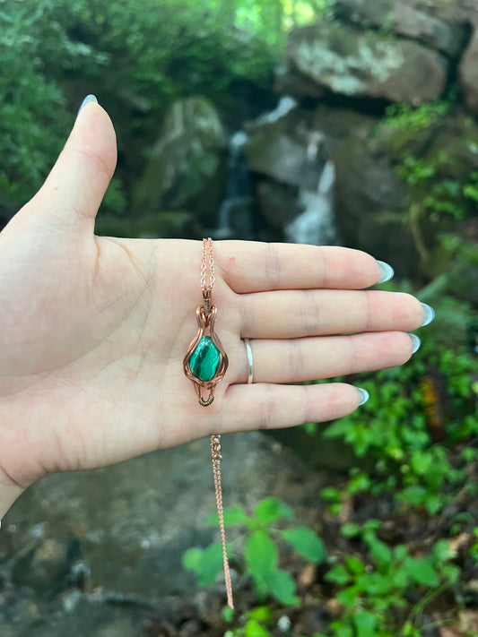 Hand holding a Wire Wrapped Malachite and Copper Necklace against a natural background
