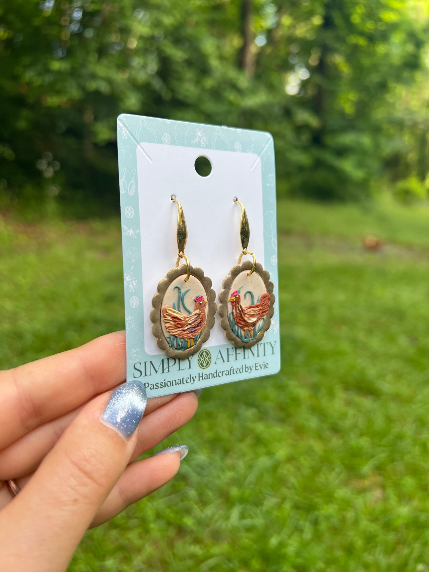chicken Earrings on a card held by a hand with a green outdoor background