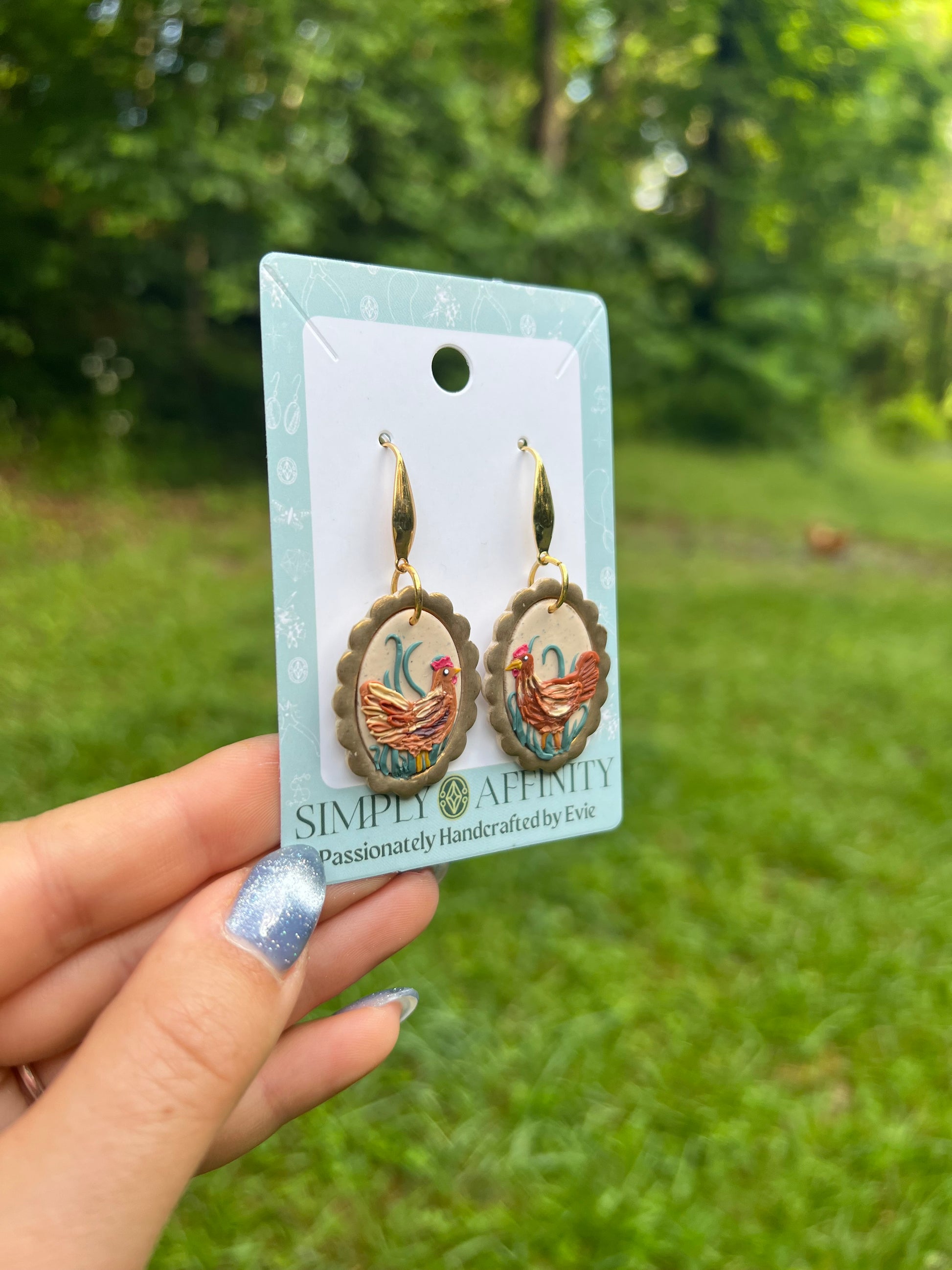 chicken Earrings on a card held by a hand with a green outdoor background