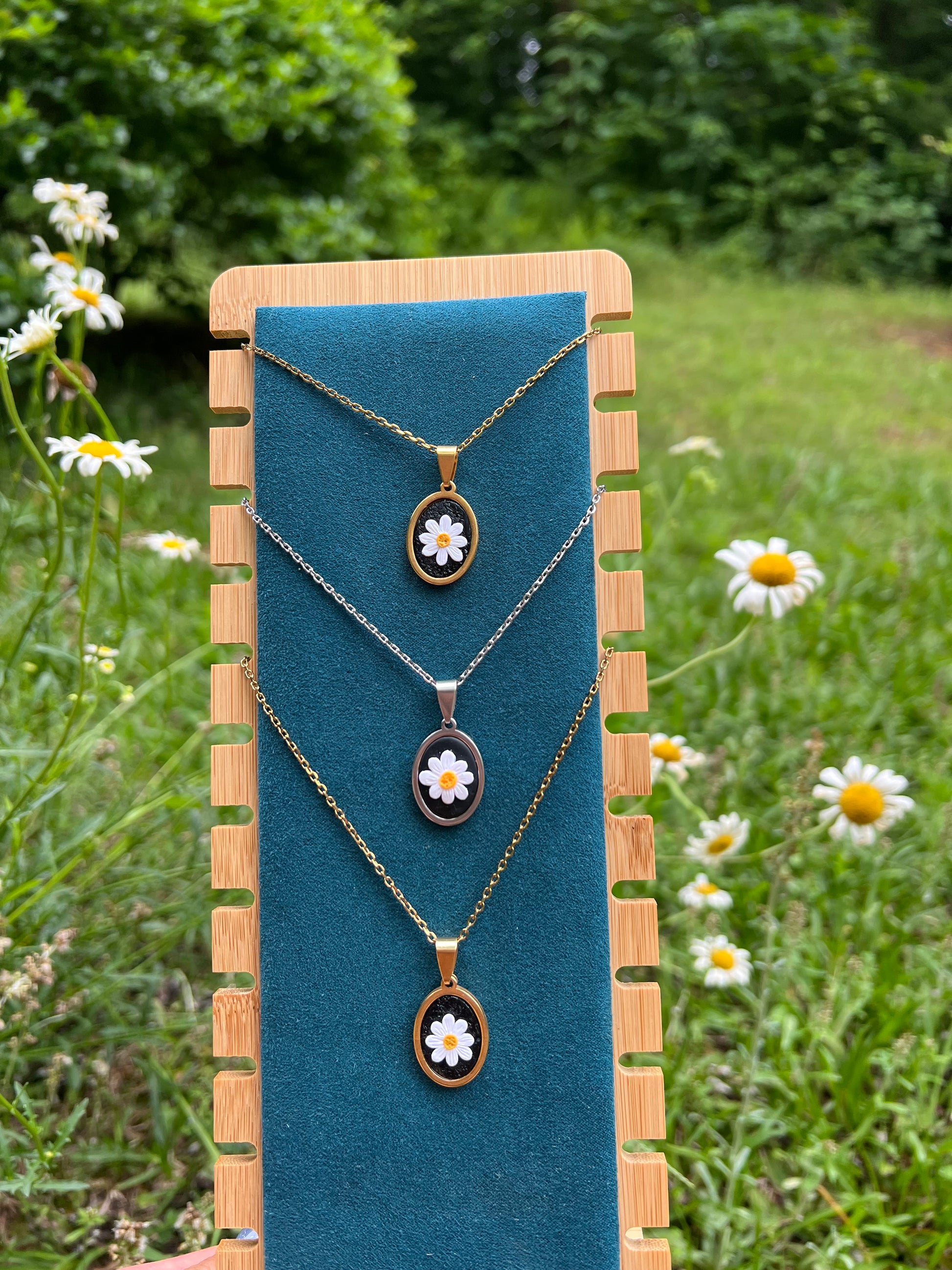 Necklace with daisy pendants on a blue cushion against a natural background with flowers.