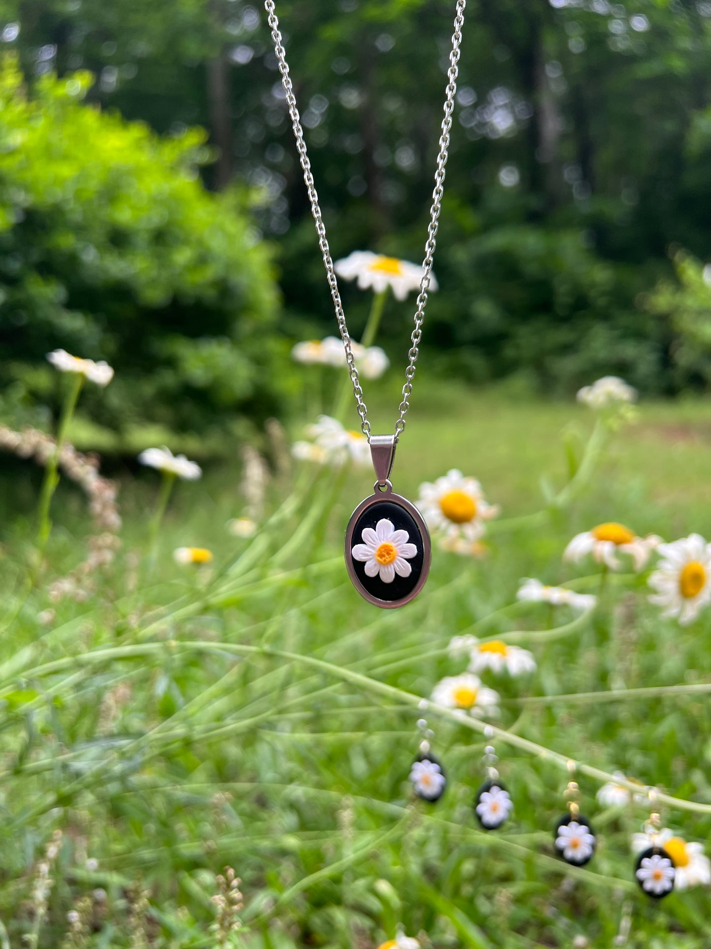 Necklace with a pendant featuring a daisy, hanging among green foliage and small white flowers.