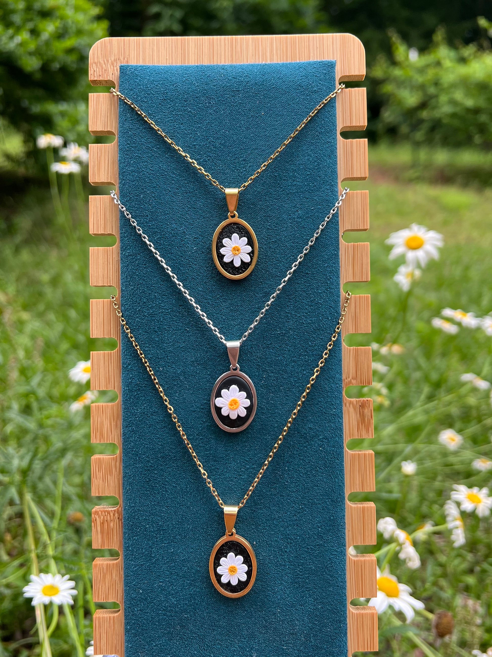 Three necklaces with daisy pendants on a blue stand with a natural background