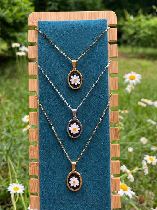 Three necklaces with daisy pendants on a blue stand with a natural background